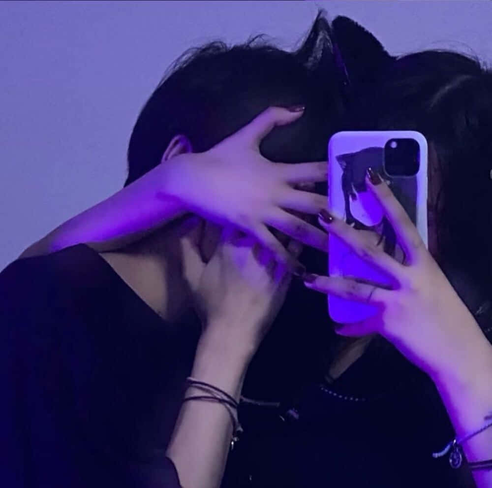 Matching Couple Profile 桌布 壁紙 — 兩個人在昏暗的紫色燈光房間中擁抱，其中一人拿著帶有貓咪手機殼的電話捕捉這一刻。