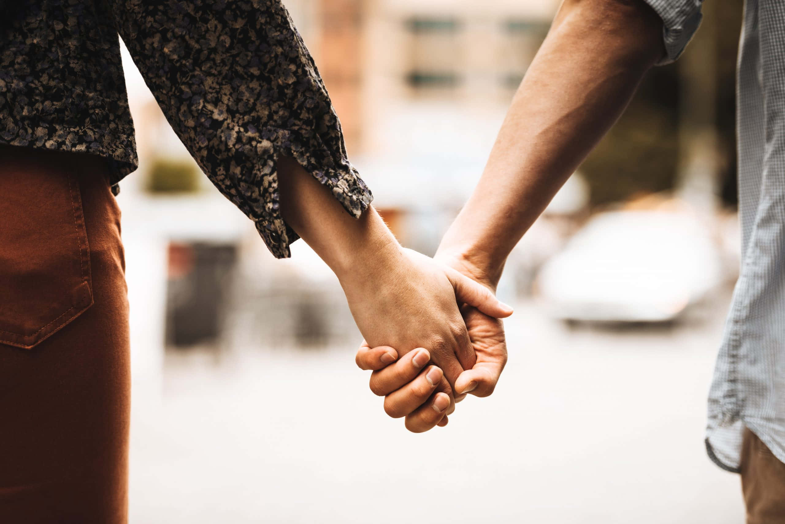 Holding Hands 桌布 壁紙 — 兩個人在模糊的城市背景下的特寫鏡頭中緊緊握住雙手。