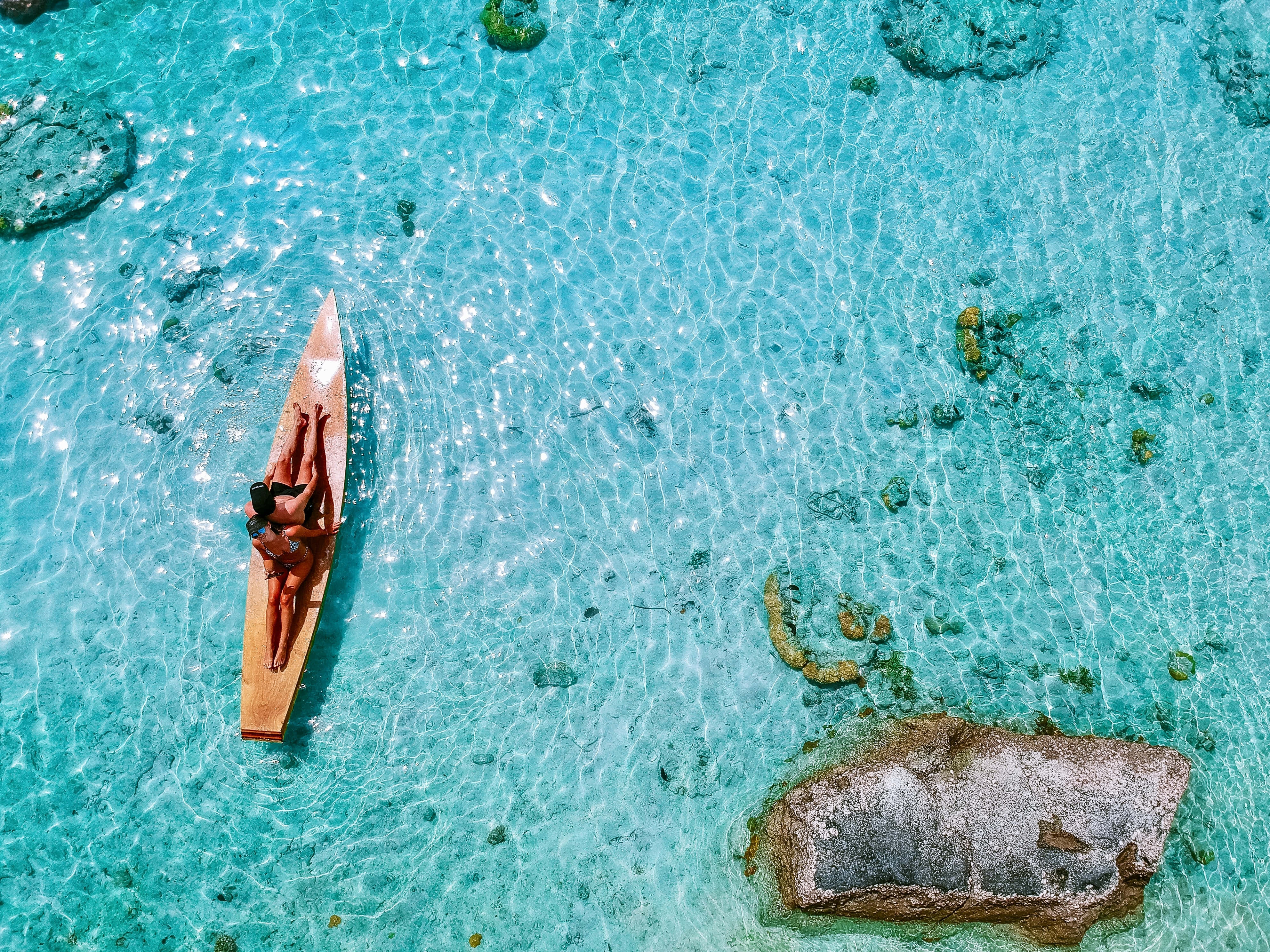 Summer Vacation 桌布 壁紙 — 兩個人在漂浮在清澈碧綠水面上的木製皮划艇上放鬆，陽光在水面上閃爍。