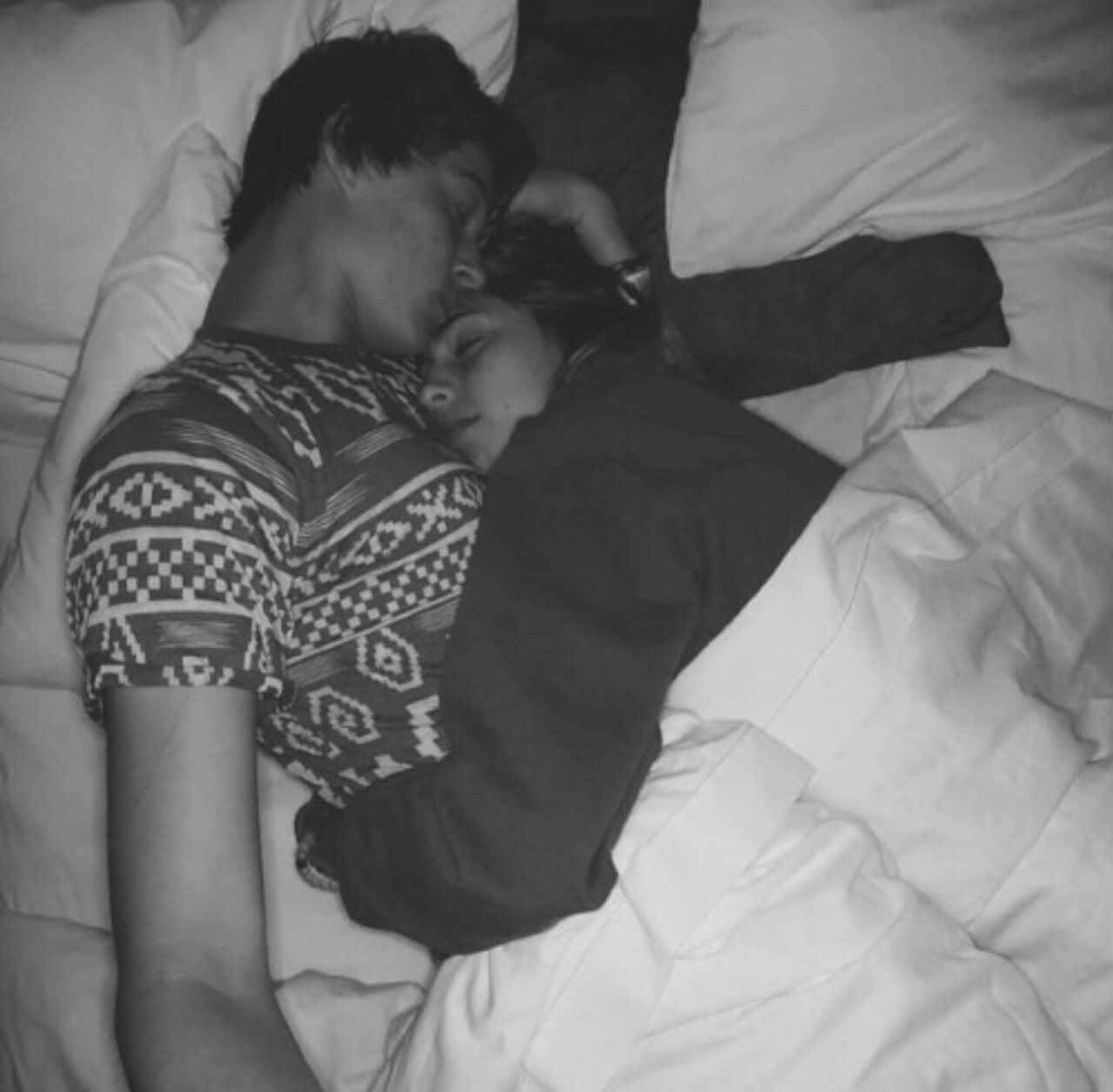 Cuddle 桌布 壁紙 — 兩個人在白色床單中纏繞著安然入睡，其中一人穿著圖案毛衣，在單色調的臥室場景中。