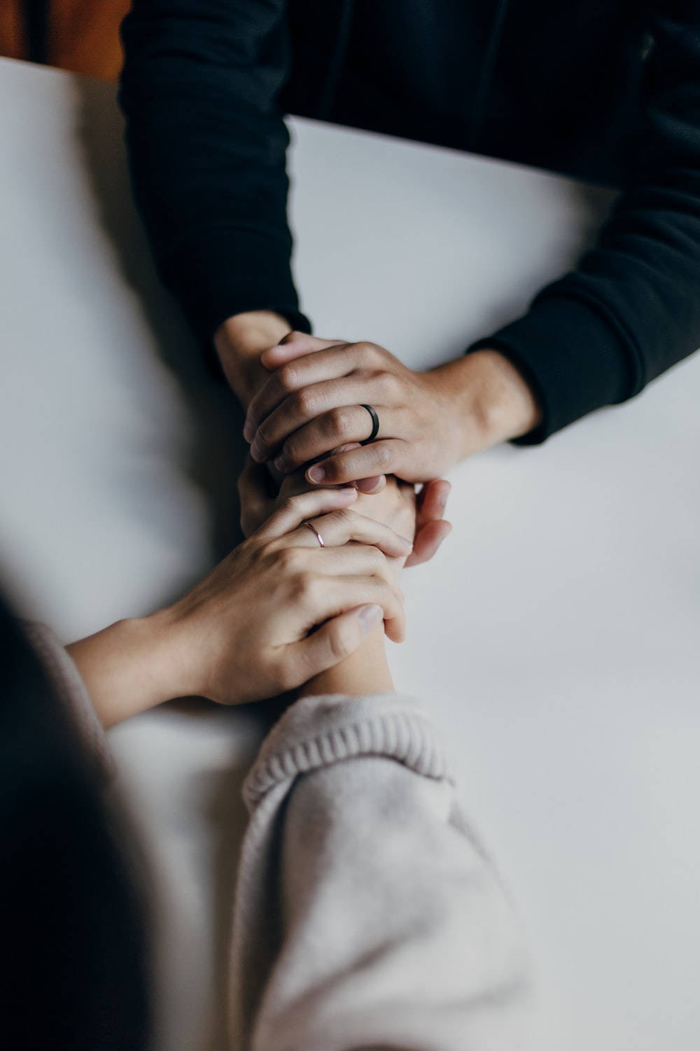 hand 桌布 壁紙 — 兩個人在白色桌子上牽手，一個人戴黑色戒指，另一個人戴銀色戒指