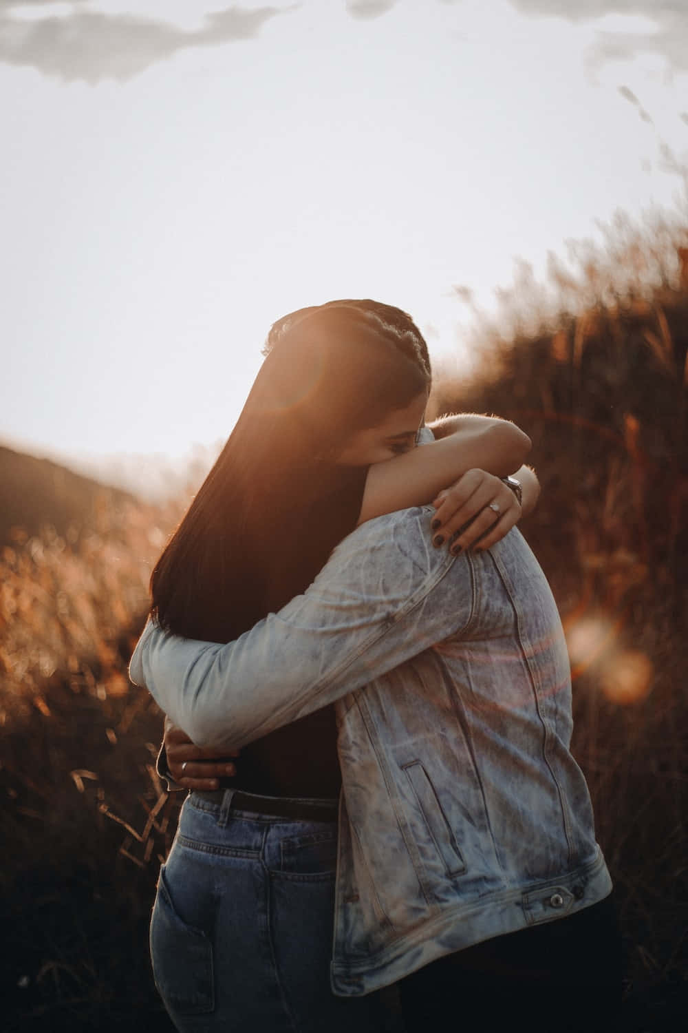 Hug 桌布 壁紙 — 兩個人在陽光明媚的田野中溫暖地擁抱，金色的光線從他們身後高高的草叢中穿過。