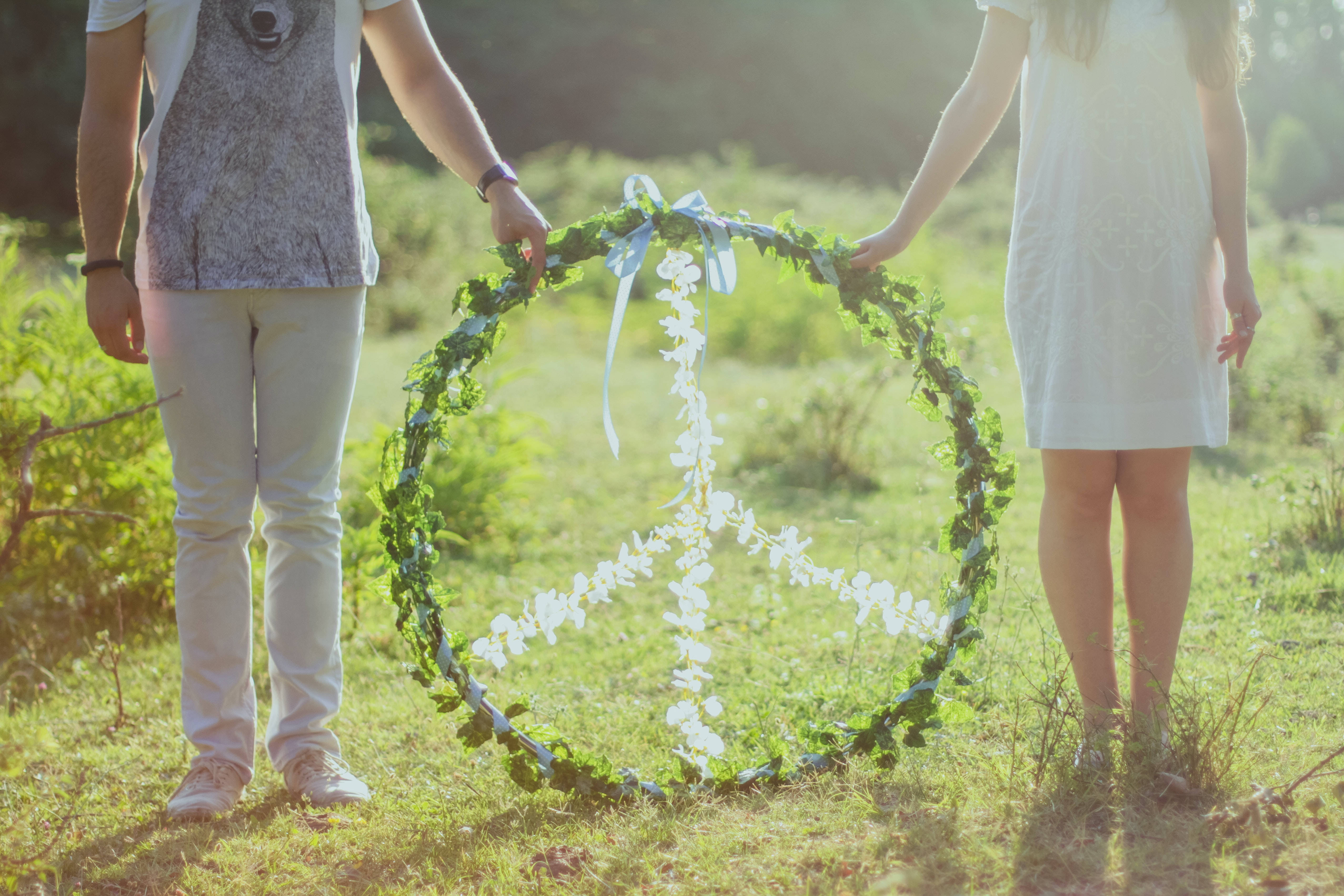 Peace Symbol 桌布 壁紙 — 兩個人在陽光明媚的草地上手持一個茂盛的綠色花環，白色花朵形成和平標誌。