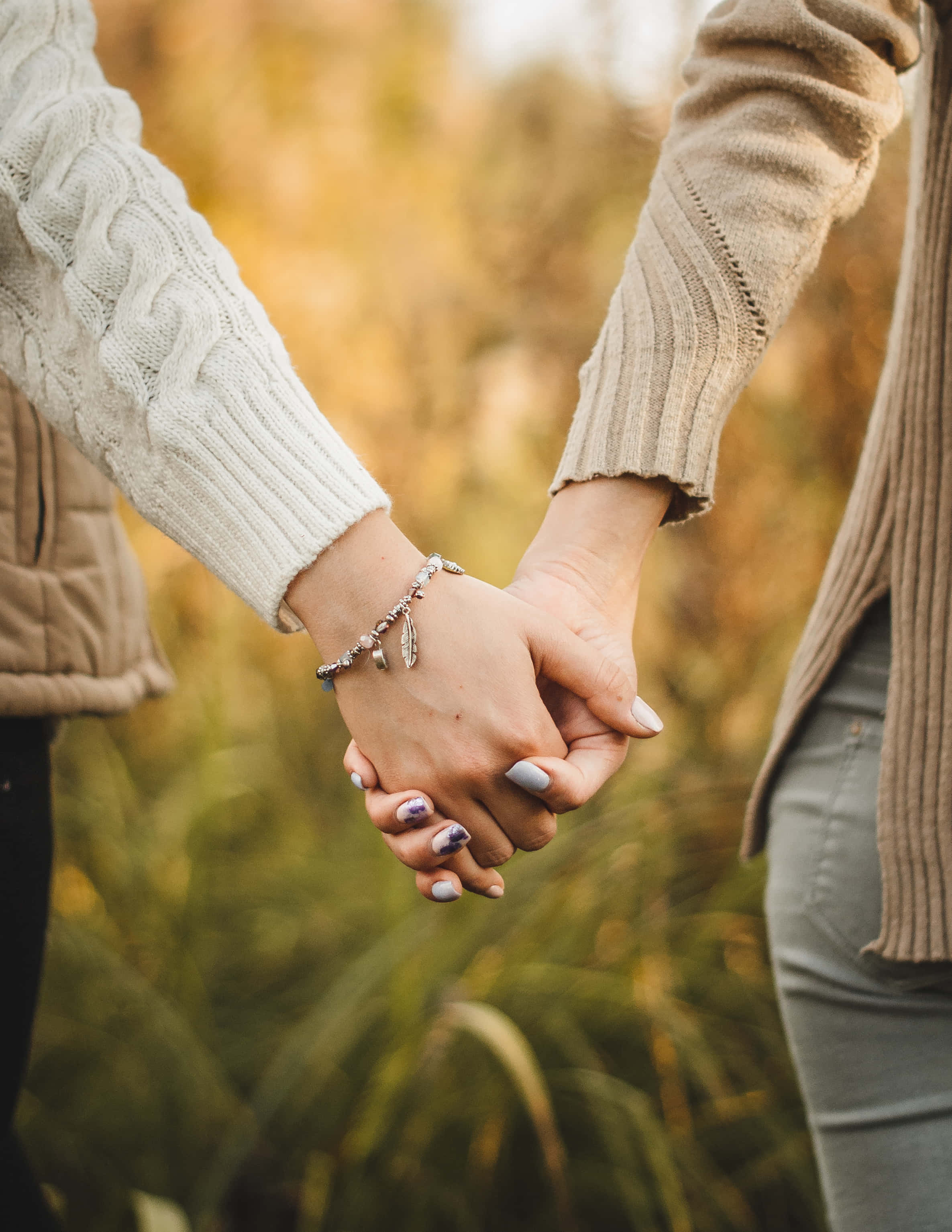 Holding Hands 桌布 壁紙 — 兩個人在陽光明媚的高草田野中牽手，穿著舒適的毛衣和塗了指甲油。