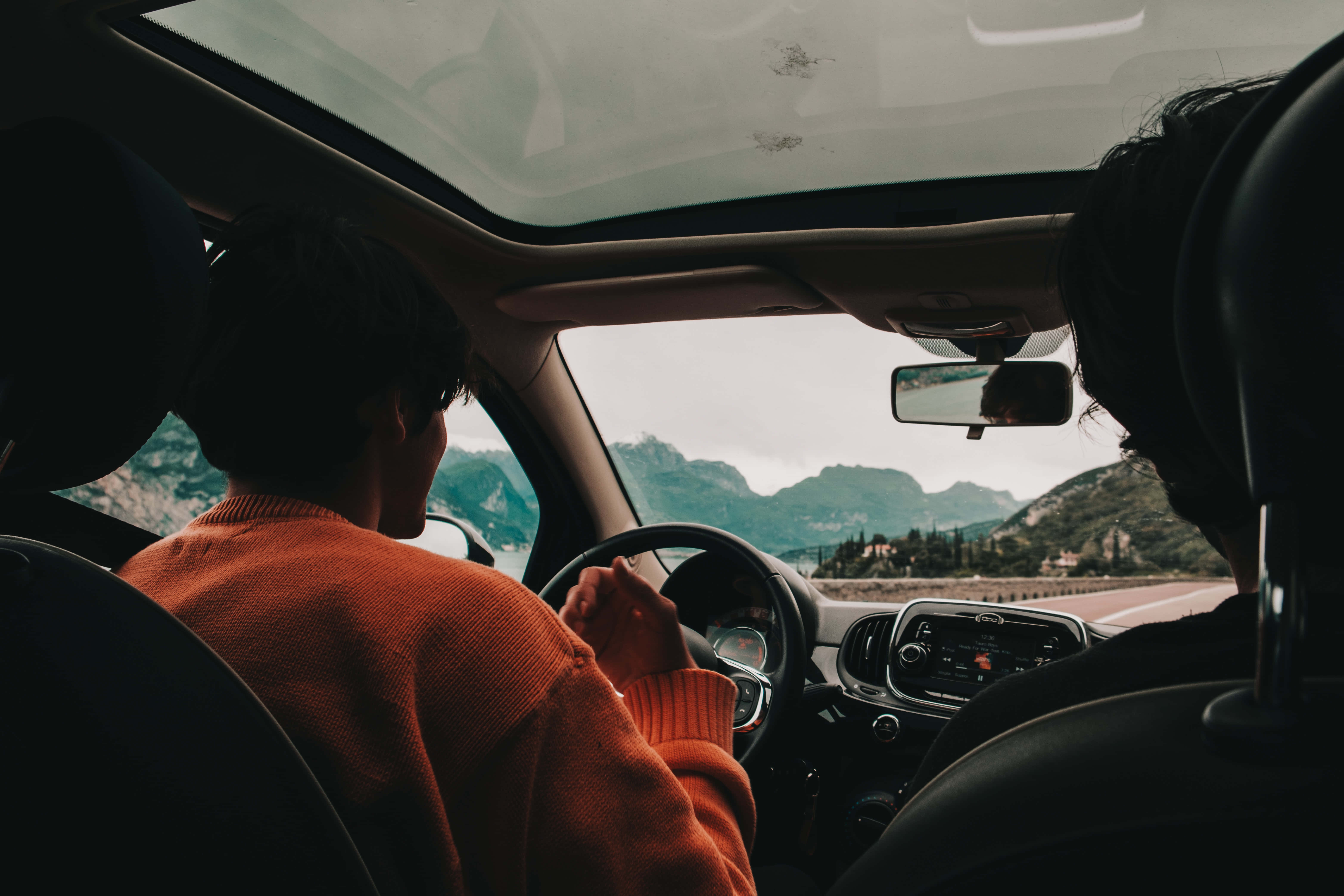 road trip 桌布 壁紙 — 兩個人坐在車內，司機身穿橙色毛衣，透過擋風玻璃凝視著山景。