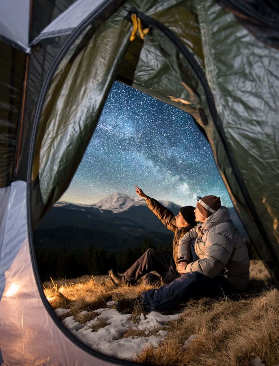 Minimalist Camping 桌布 壁紙 — 兩個人坐在雪峰上的帳篷內，指向頭頂的銀河系。