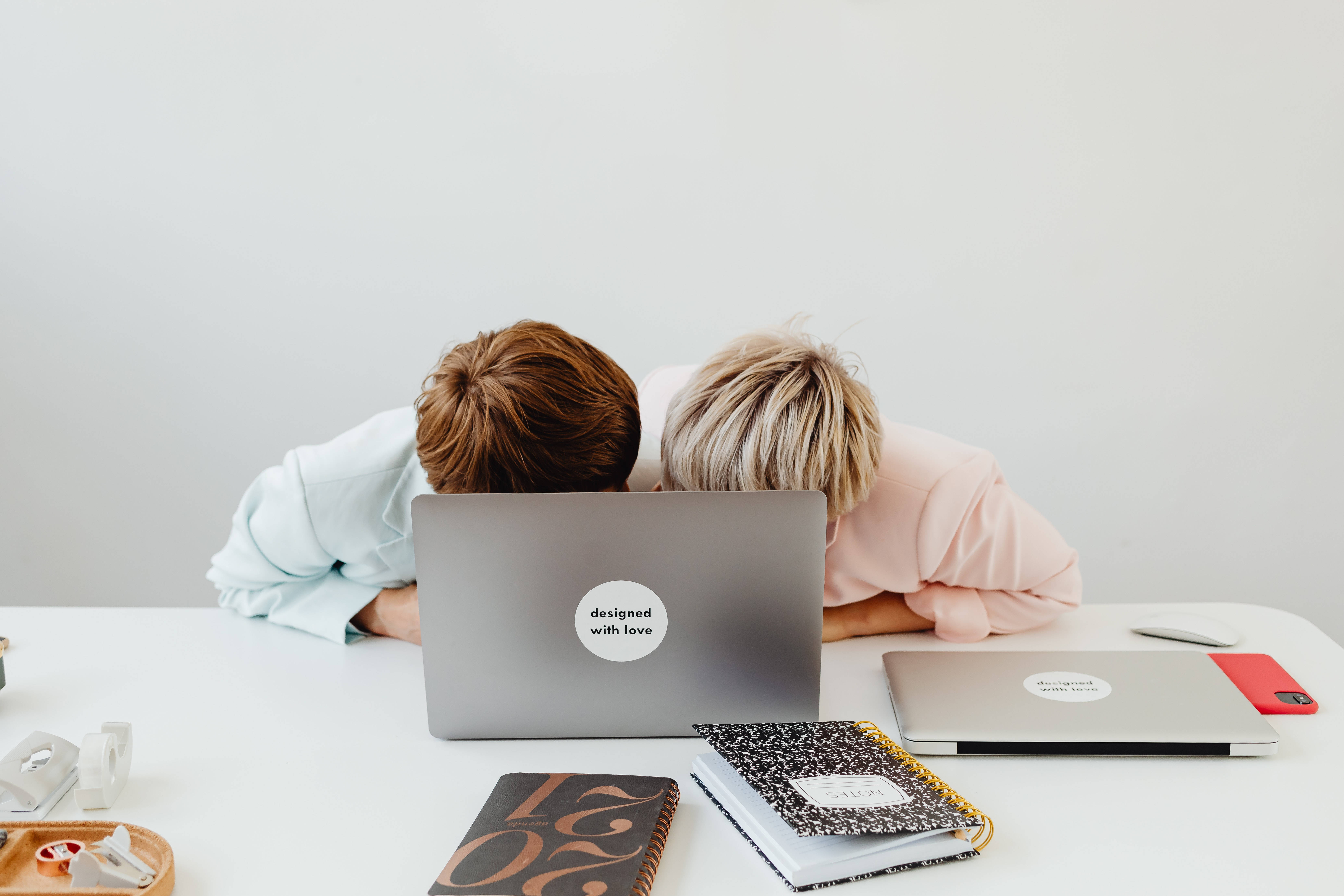 aesthetic tumblr laptop 桌布 壁紙 — 兩個人將頭靠在筆記型電腦上，周圍是簡約白色辦公桌，上面放著筆記本和辦公用品。