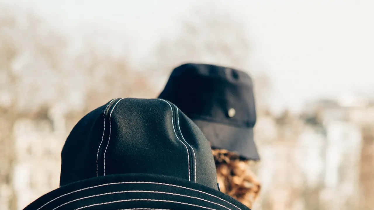 Clothes 桌布 壁紙 — 兩個人戴著帶有白色縫線的深色帽子，背對背站在柔和模糊的城市背景下。