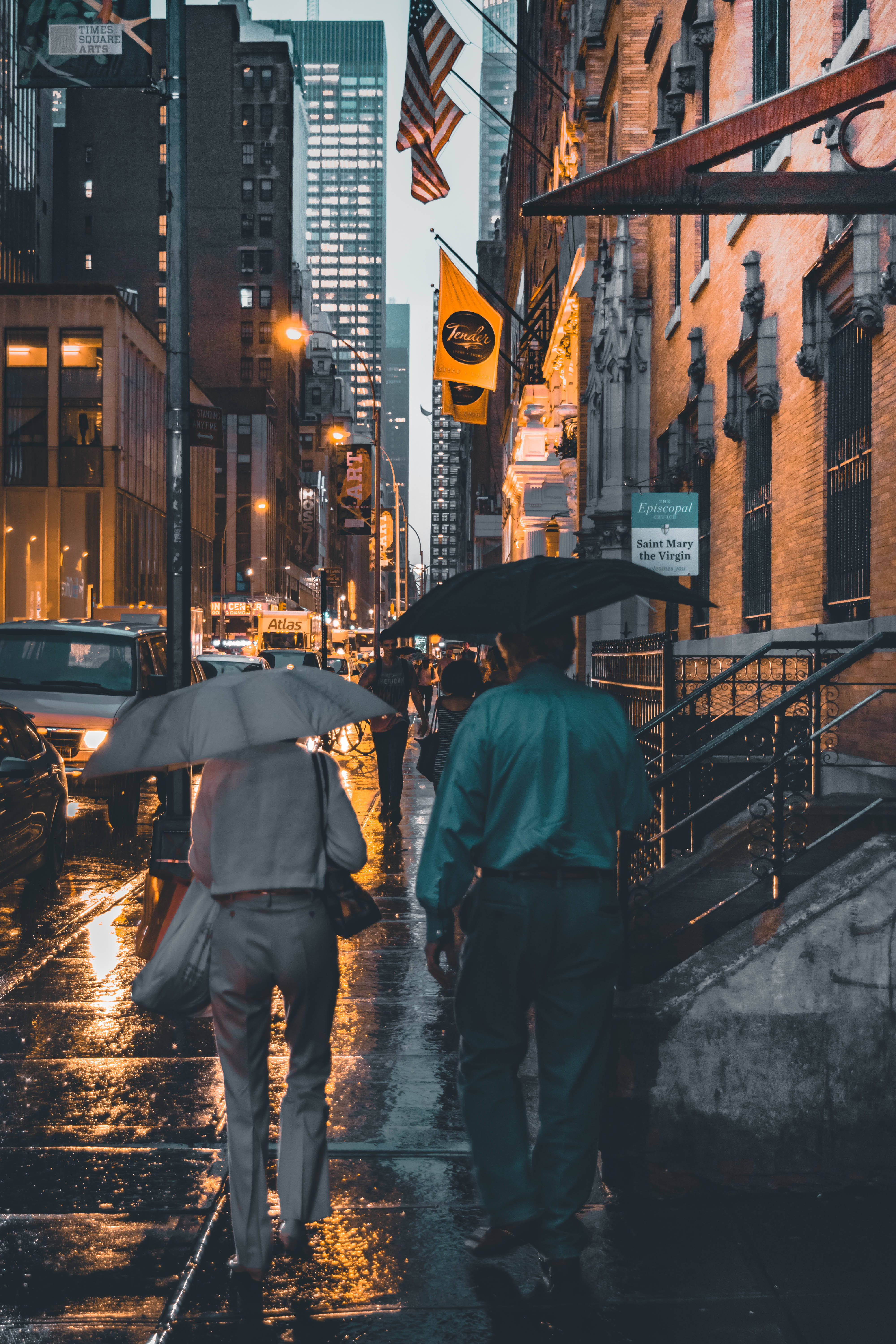 桌布 壁紙 — 兩個人撐著雨傘在夜晚濕漉漉的街道上行走，映照著溫暖的路燈和建築物招牌。