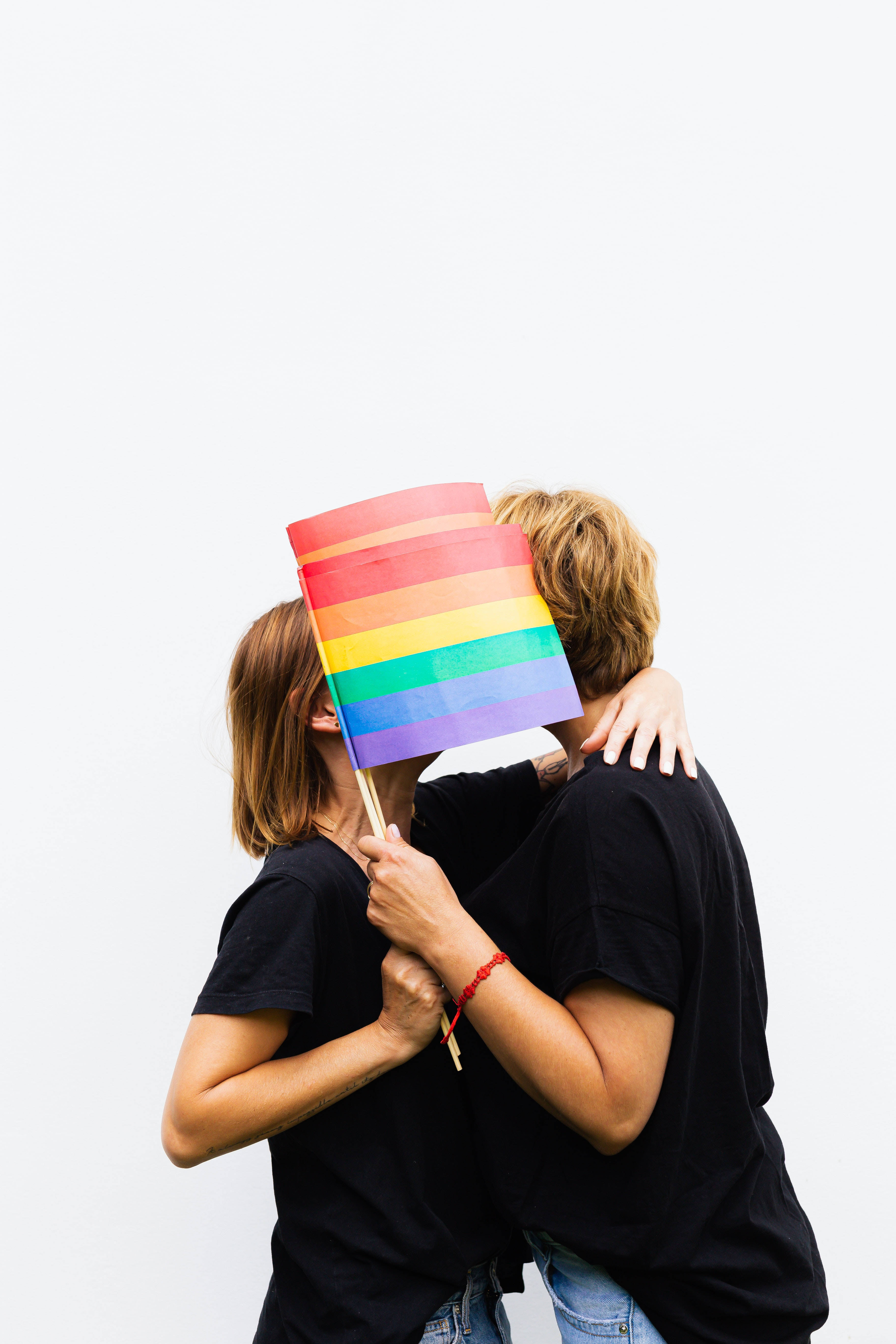 Lesbian Flag 桌布 壁紙 — 兩個人擁抱，同時將彩虹旗舉過臉龐，背景為純白色。