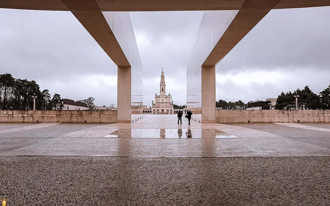 Portugal 桌布 壁紙 — 兩個人物在潮濕陰天的日子，在廣闊的混凝土天篷下走向遠處的華麗教堂。