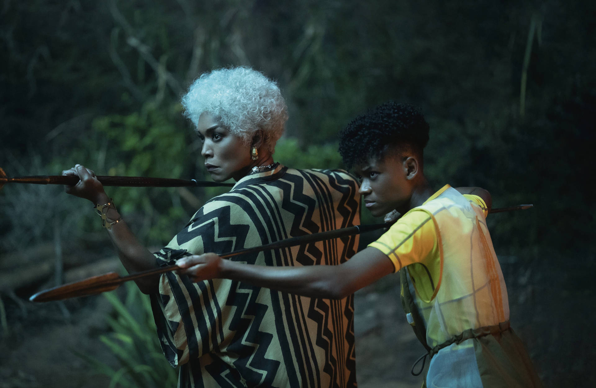 Wakanda 桌布 壁紙 — 兩個人物手持弓箭，在昏暗的森林中保持警覺，一個銀髮披肩、身穿圖案長袍，另一個穿著黃色襯衫，兩人都專注地注視前方。