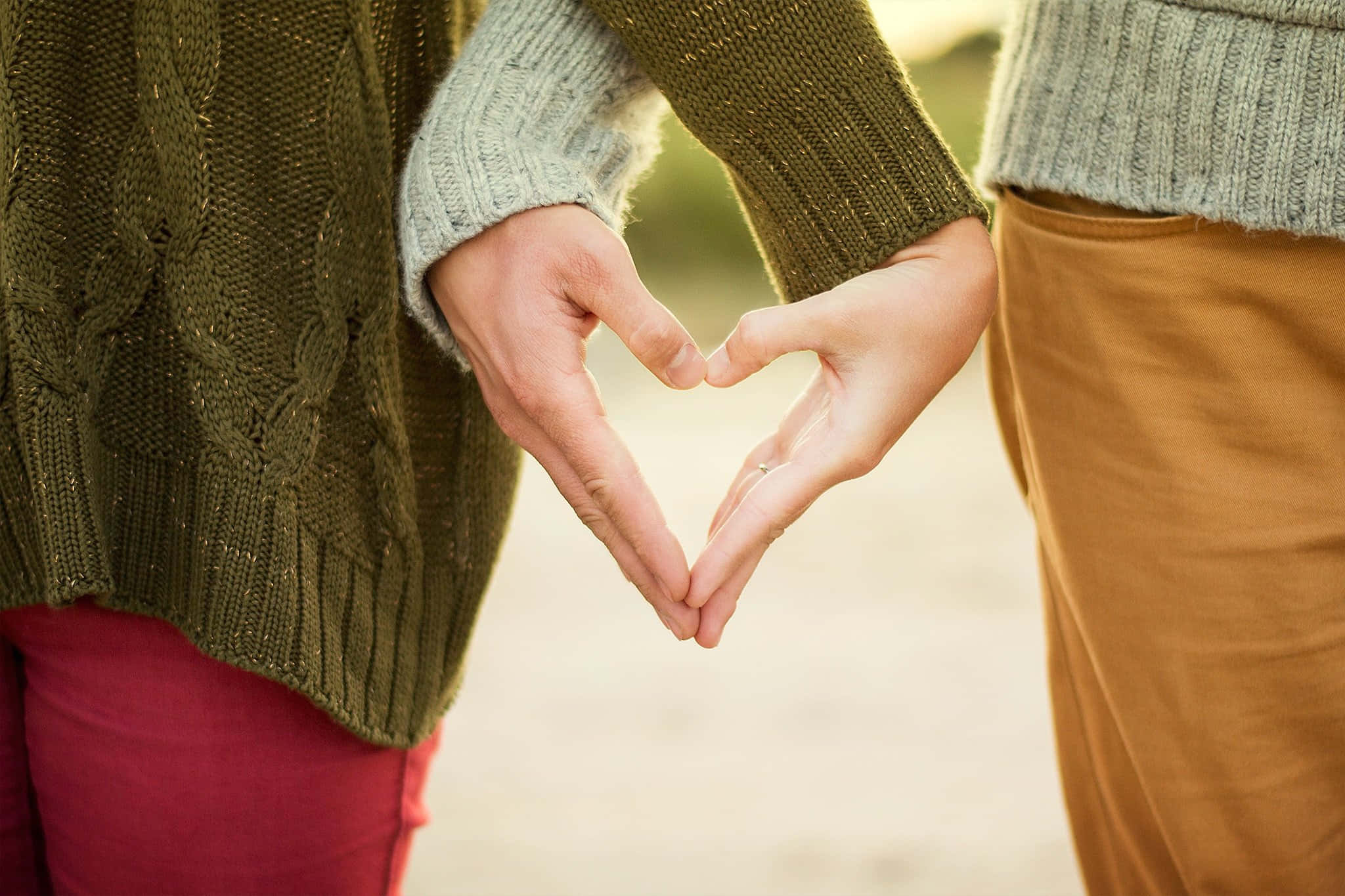 Romance 桌布 壁紙 — 兩個人用雙手形成心形，背景是柔和模糊的戶外景色。