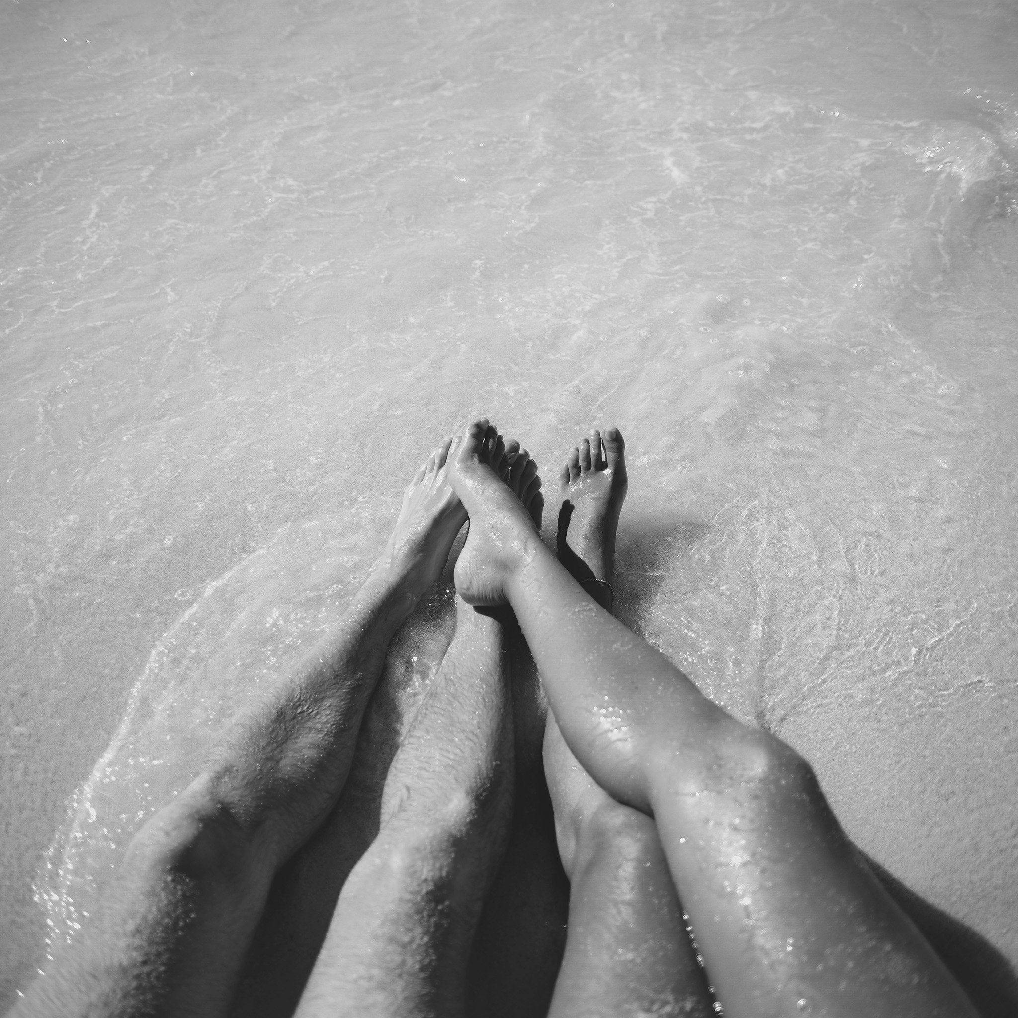 couple cuddle 桌布 壁紙 — 兩個人的腿在淺海水中一起休息，以單色捕捉，伴隨著溫柔的波浪。