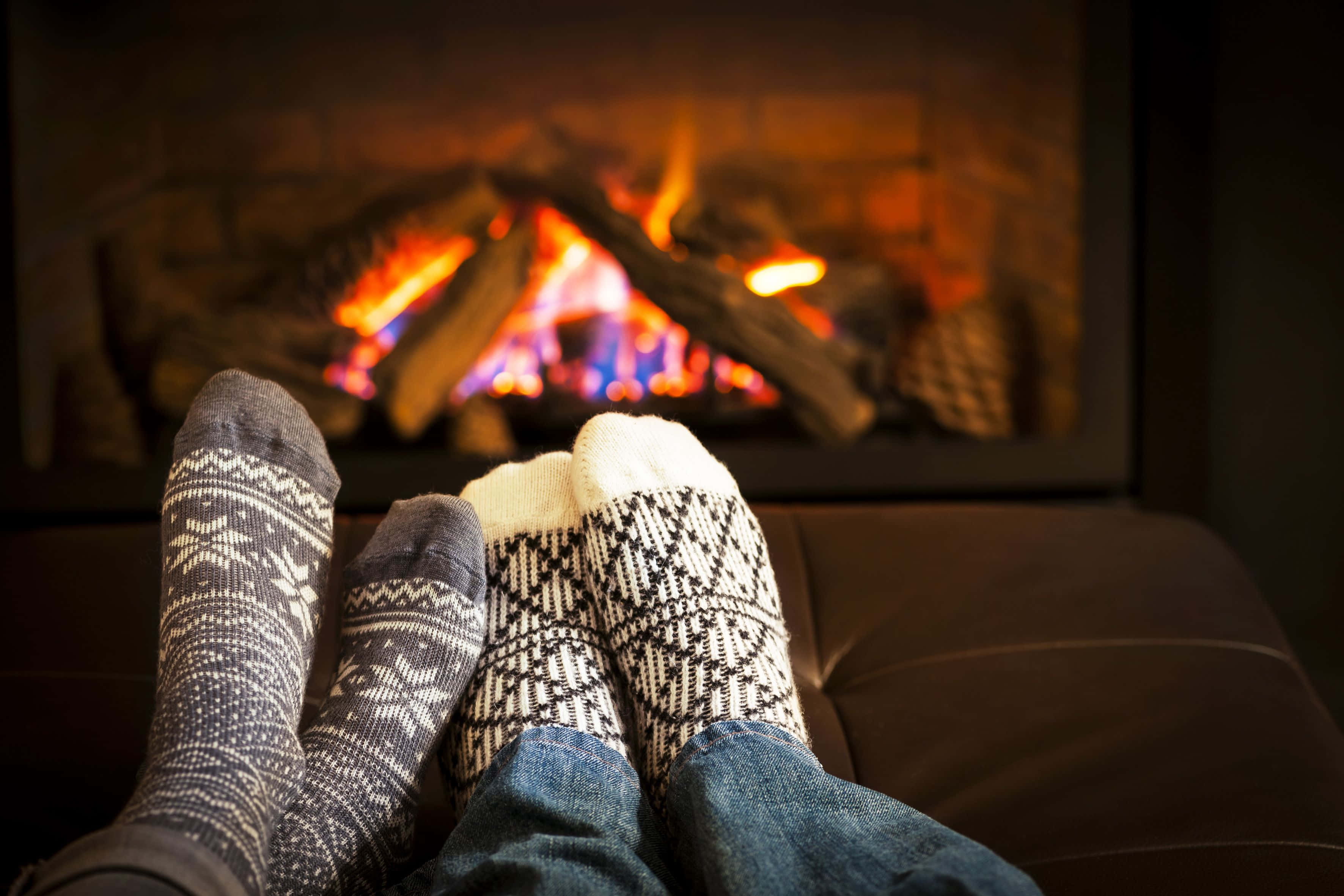 Cozy Fire 桌布 壁紙 — 兩個人穿著圖案襪子，翹起雙腳，在溫暖噼啪作響的壁爐前放鬆。