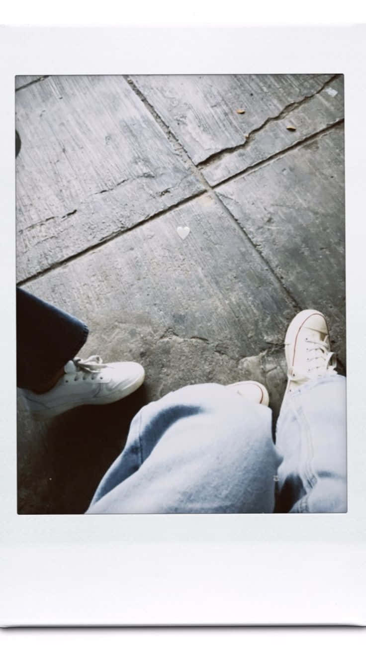 Aesthetic Polaroid 桌布 壁紙 — 兩個人穿著白色運動鞋和牛仔褲坐在裂開的混凝土上，地上畫著一個小小的白色心形。