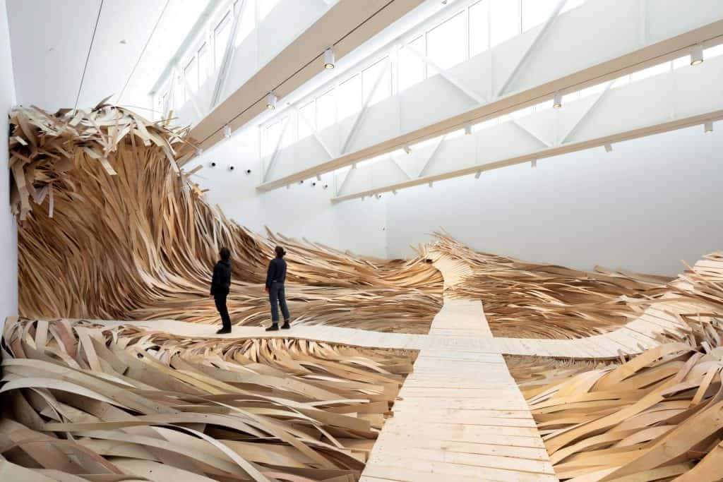Installation Art 桌布 壁紙 — 兩個人站在一條木製步道上，穿過一個由層壓木材製成的巨大波浪雕塑，位於明亮的白色畫廊中。