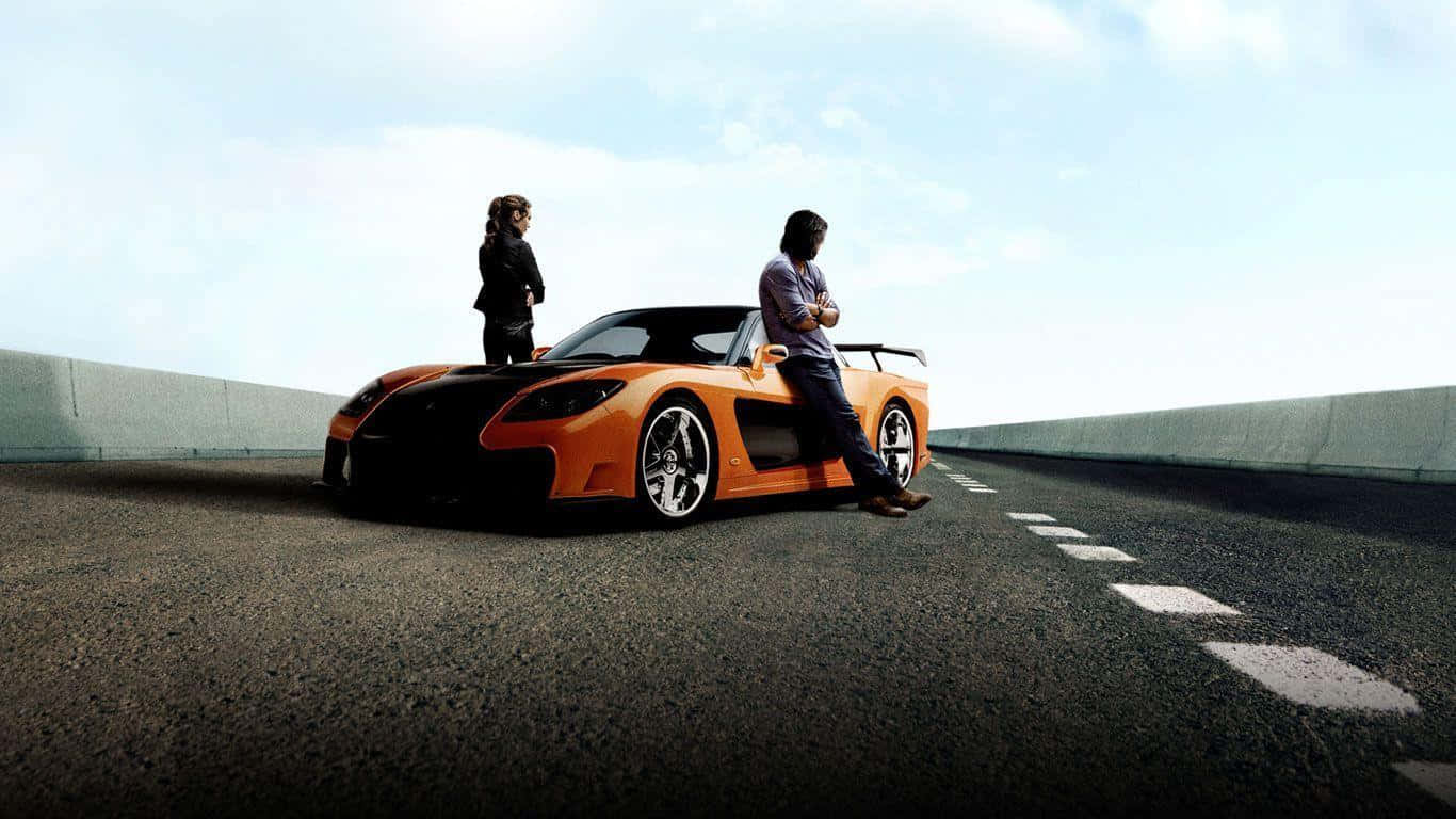 Fast And Furious 桌布 壁紙 — 兩個人站在一輛鮮橙色跑車旁邊，跑車停在空蕩蕩的高速公路上，天空明亮。