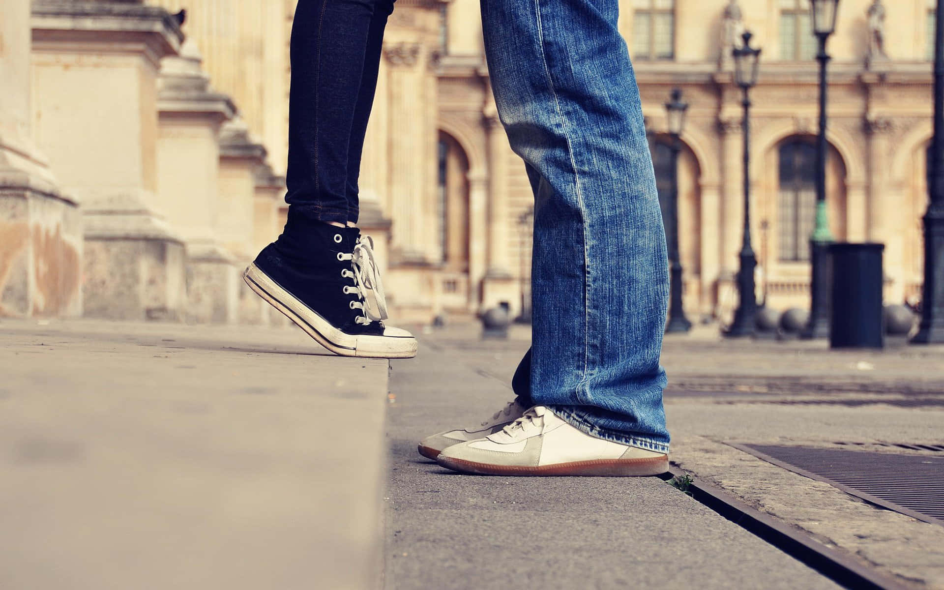 Lovers 桌布 壁紙 — 兩個人站在城市街道上，一隻腳踩在邊緣，穿著對比鮮明的運動鞋和牛仔褲，背景是歷史建築。