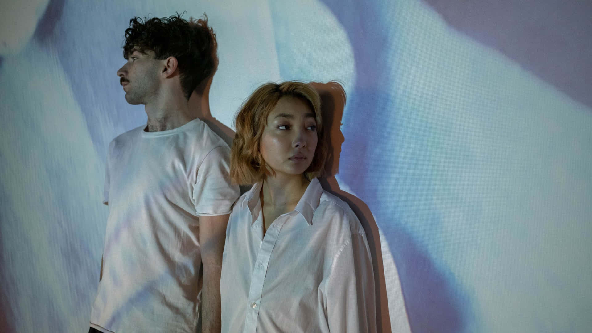 Sad Couple 桌布 壁紙 — 兩個人背對背站立，背景是柔和燈光的抽象牆壁，帶有冷色調的藍色和紫色。