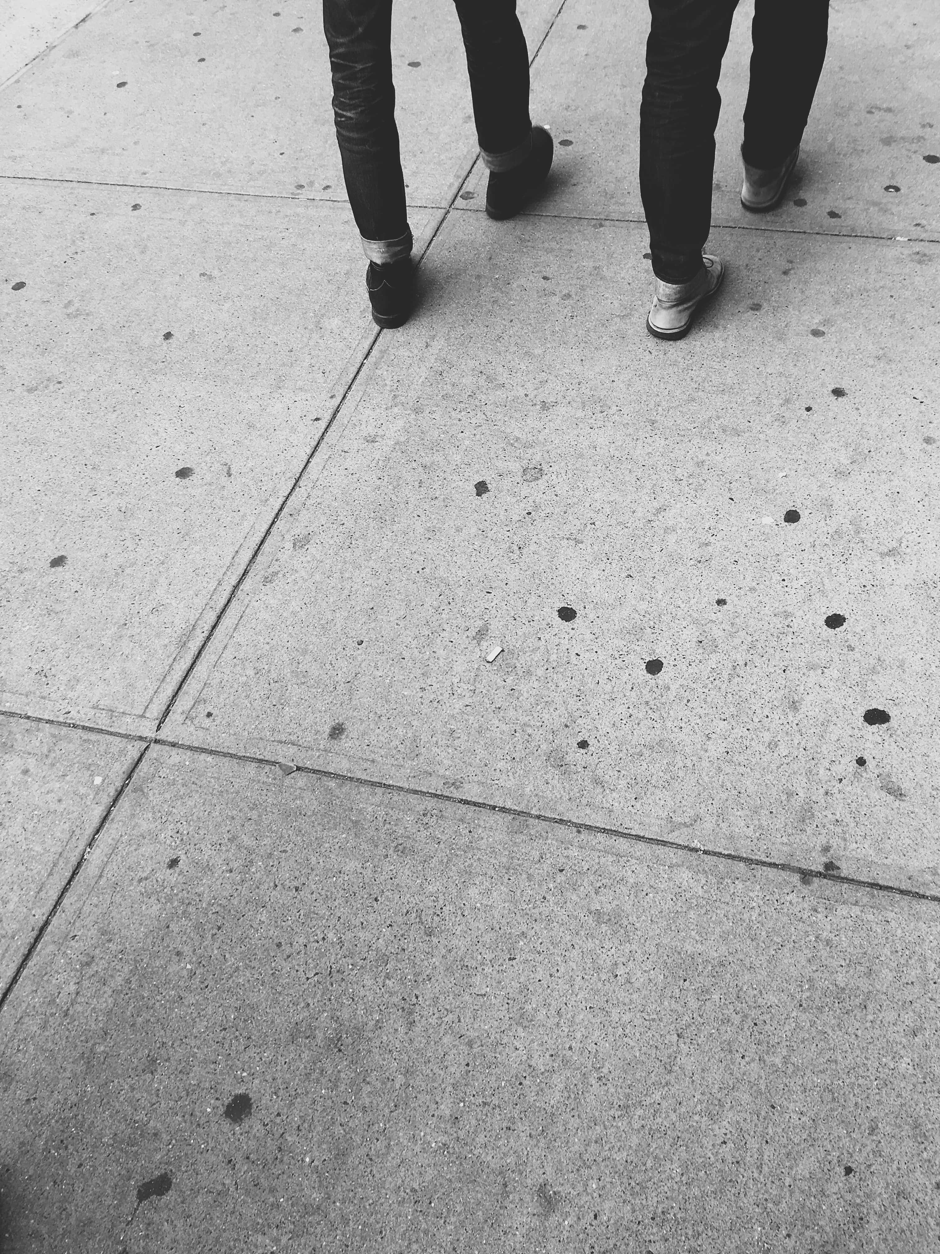 Sidewalk 桌布 壁紙 — 兩個人走在裂開的混凝土人行道上，以單色調從低角度捕捉他們的鞋子和牛仔褲。
