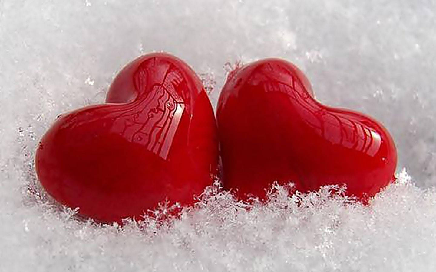 愛心 桌布 壁紙 — 兩個光滑的紅色心形物體依偎在柔軟的白雪中，帶有清晰的晶體質感。