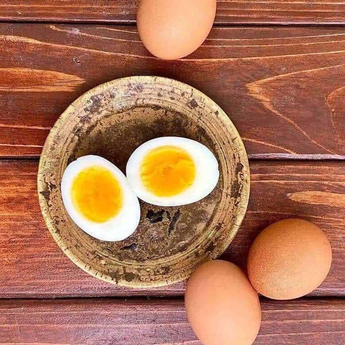 Egg 桌布 壁紙 — 兩個切半的水煮蛋，蛋黃鮮豔，放在一個質樸的碗裡，置於木質表面上，周圍環繞著完整的雞蛋。