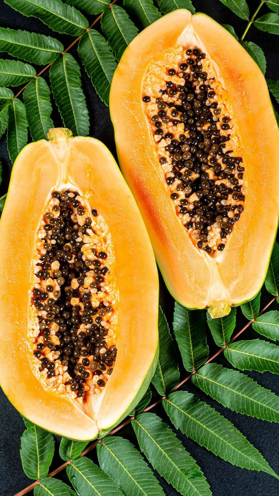 Fruits 桌布 壁紙 — 兩個切半的番石榴帶有黑色種子，放在鮮綠色的葉子上，背景深色。