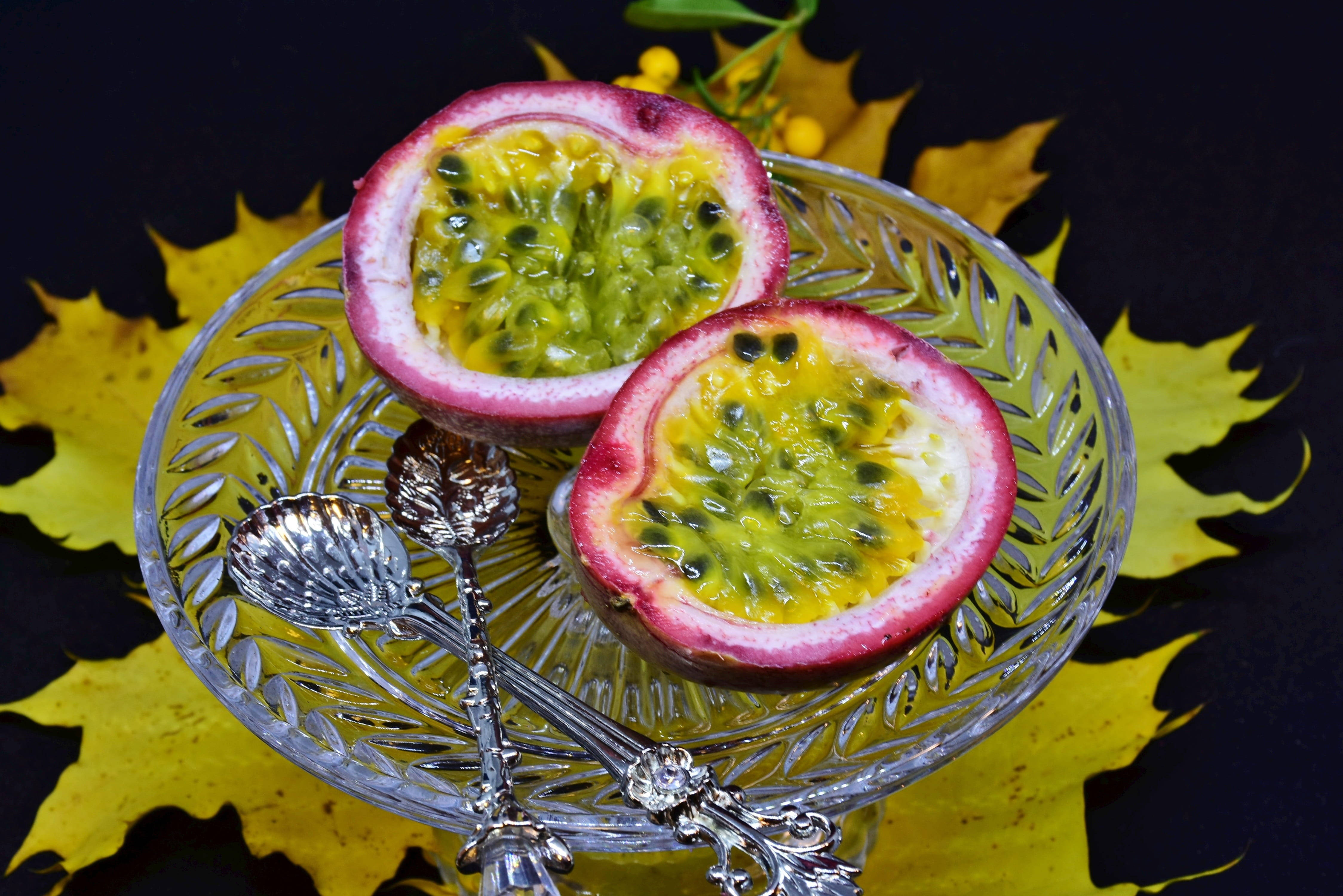 Food Photography 桌布 壁紙 — 兩個切半的百香果，帶有 juicy 的種子，放在一個水晶碗中，置於黃色楓葉上，背景為深色。