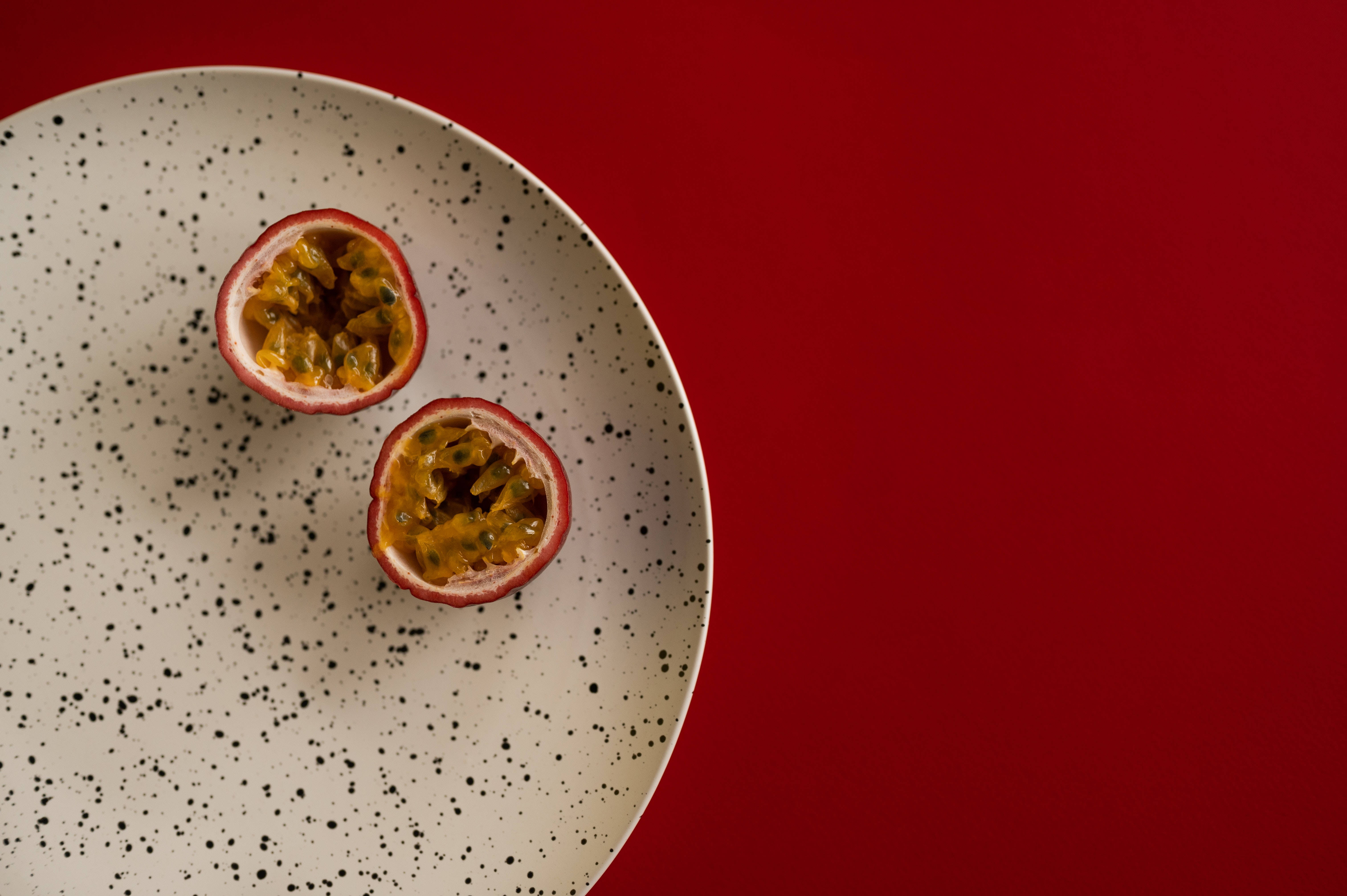 Food Photography 桌布 壁紙 — 兩個切半的百香果，帶有多汁的種子，放在一個有斑點的盤子上，背景是鮮豔的紅色。