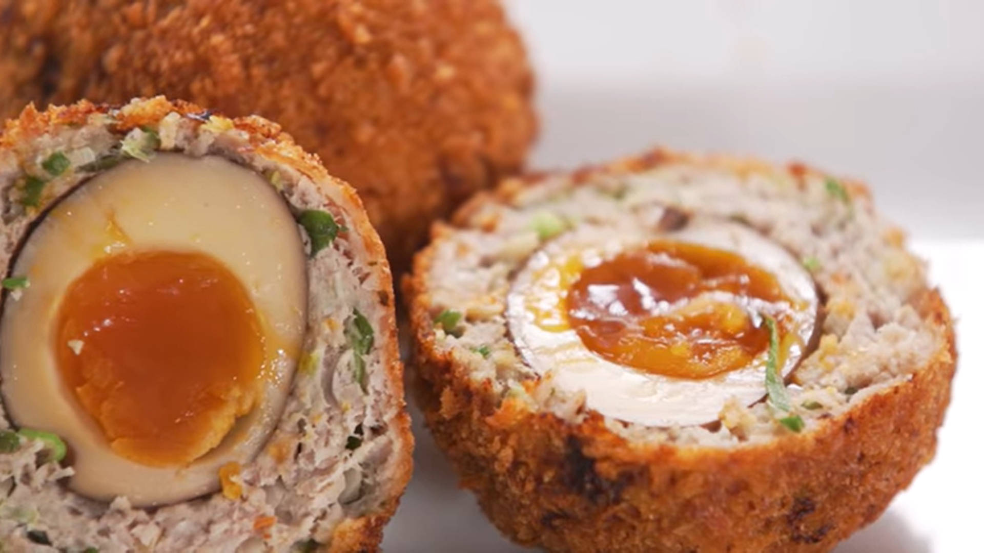 Egg 桌布 壁紙 — 兩個切半的蘇格蘭蛋特寫，露出流心蛋黃和酥脆的麵包粉外層。