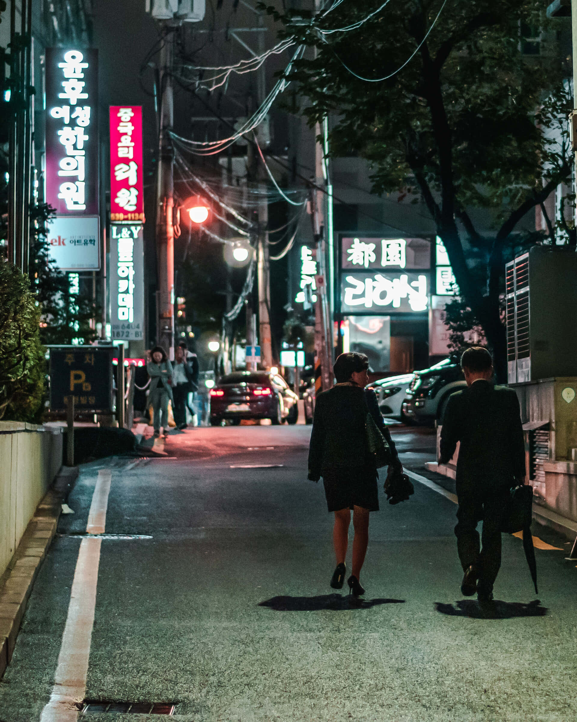 暗黑風格 桌布 壁紙 — 兩個剪影人物在夜晚走在一條霓虹燈照亮的韓國街道上，頭頂有發光的招牌和纏繞的電線。