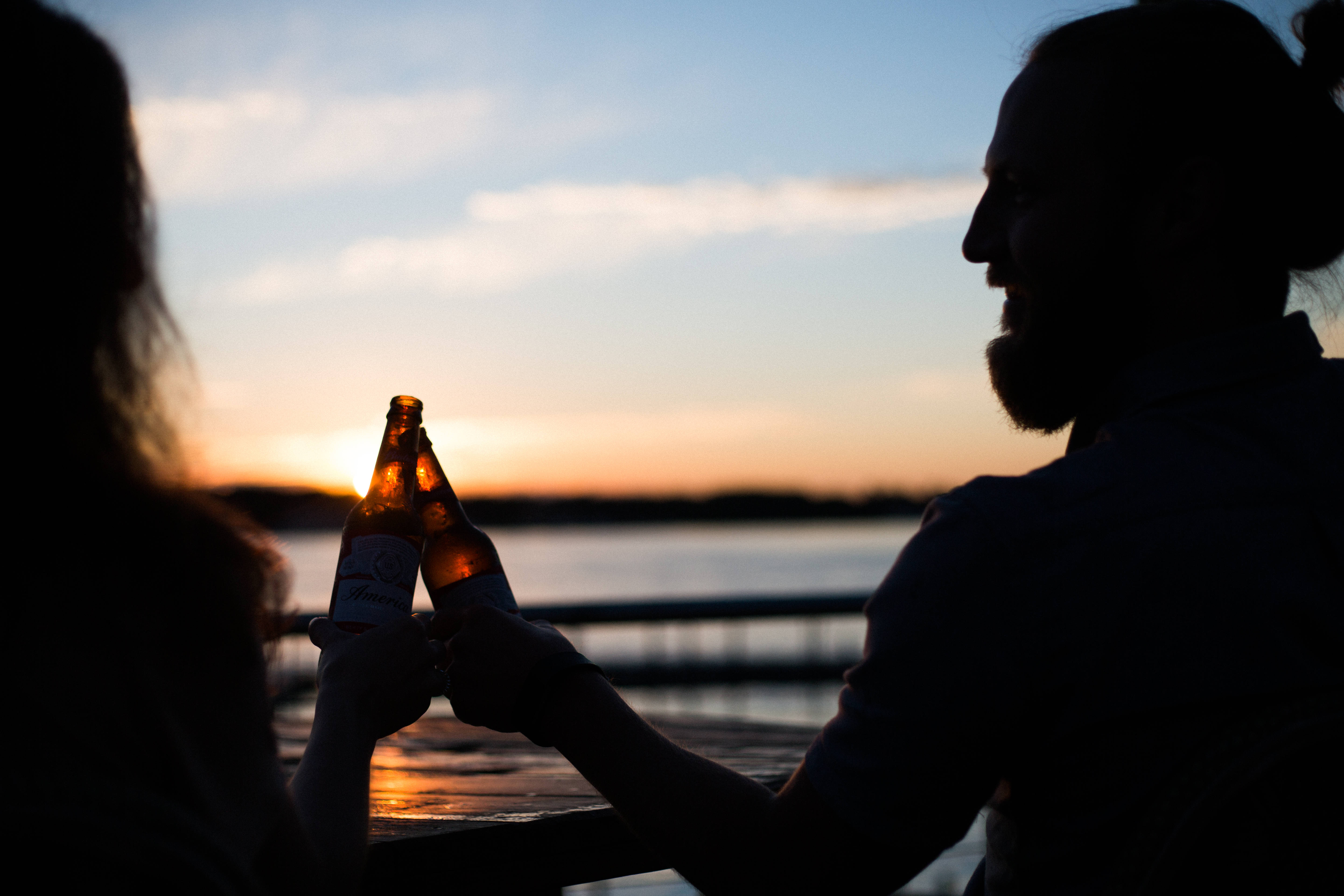 Cheers 桌布 壁紙 — 兩個剪影人物在平靜的水天相接處日落時分碰啤酒瓶。