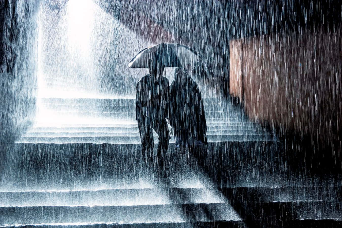 Raining 桌布 壁紙 — 兩個剪影人物在明亮的頭頂燈光下，共用一把雨傘走下濕滑的樓梯。