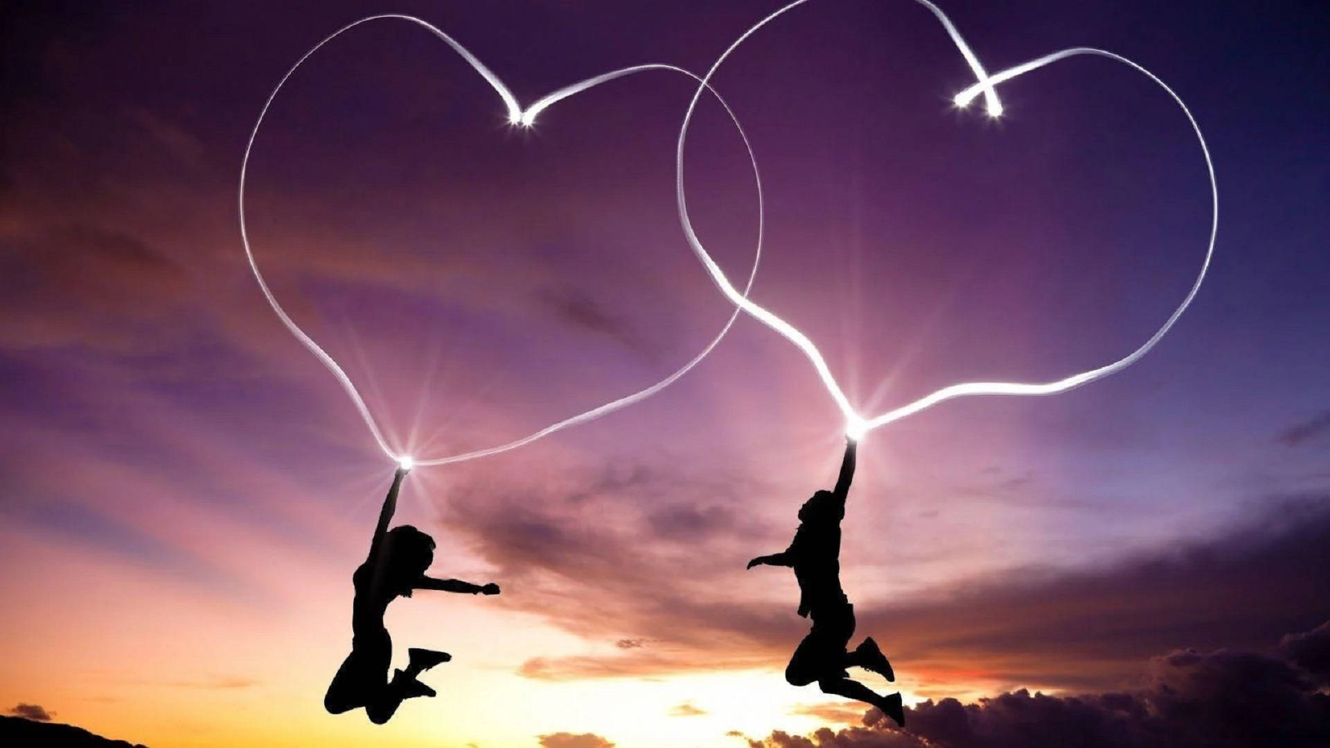 Romantic Love 桌布 壁紙 — 兩個剪影人物在暮色天空下歡快地跳躍，用發光棒畫出心形圖案。