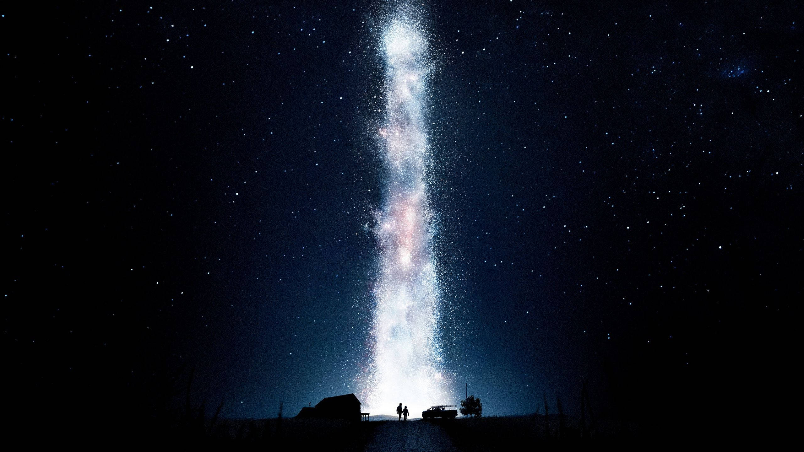 星際效應 桌布 壁紙 — 兩個剪影人物站在一座高聳、發光的星系下方，該星系垂直劃過繁星點點的夜空。