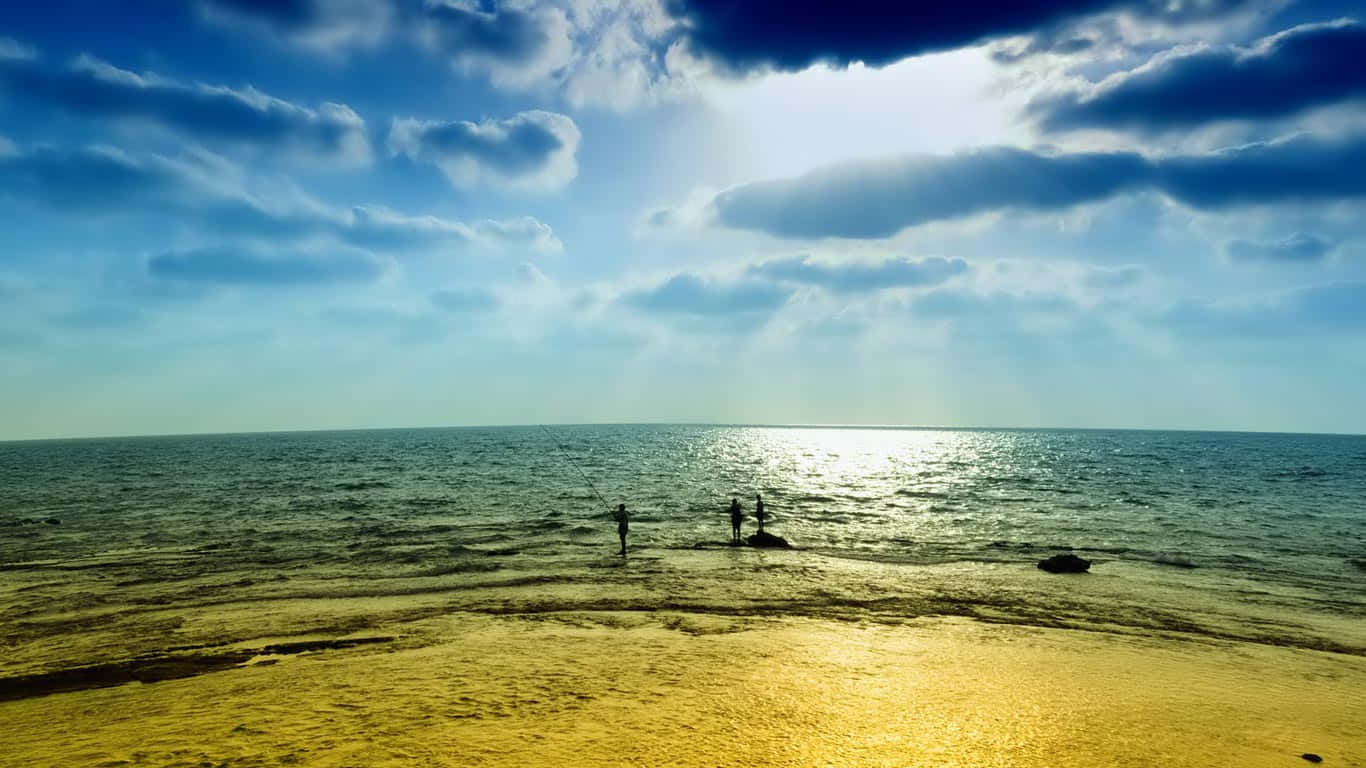 海灘 桌布 壁紙 — 兩個剪影人物站在海邊，陽光穿過戲劇性的雲層，灑在金色的沙灘上。