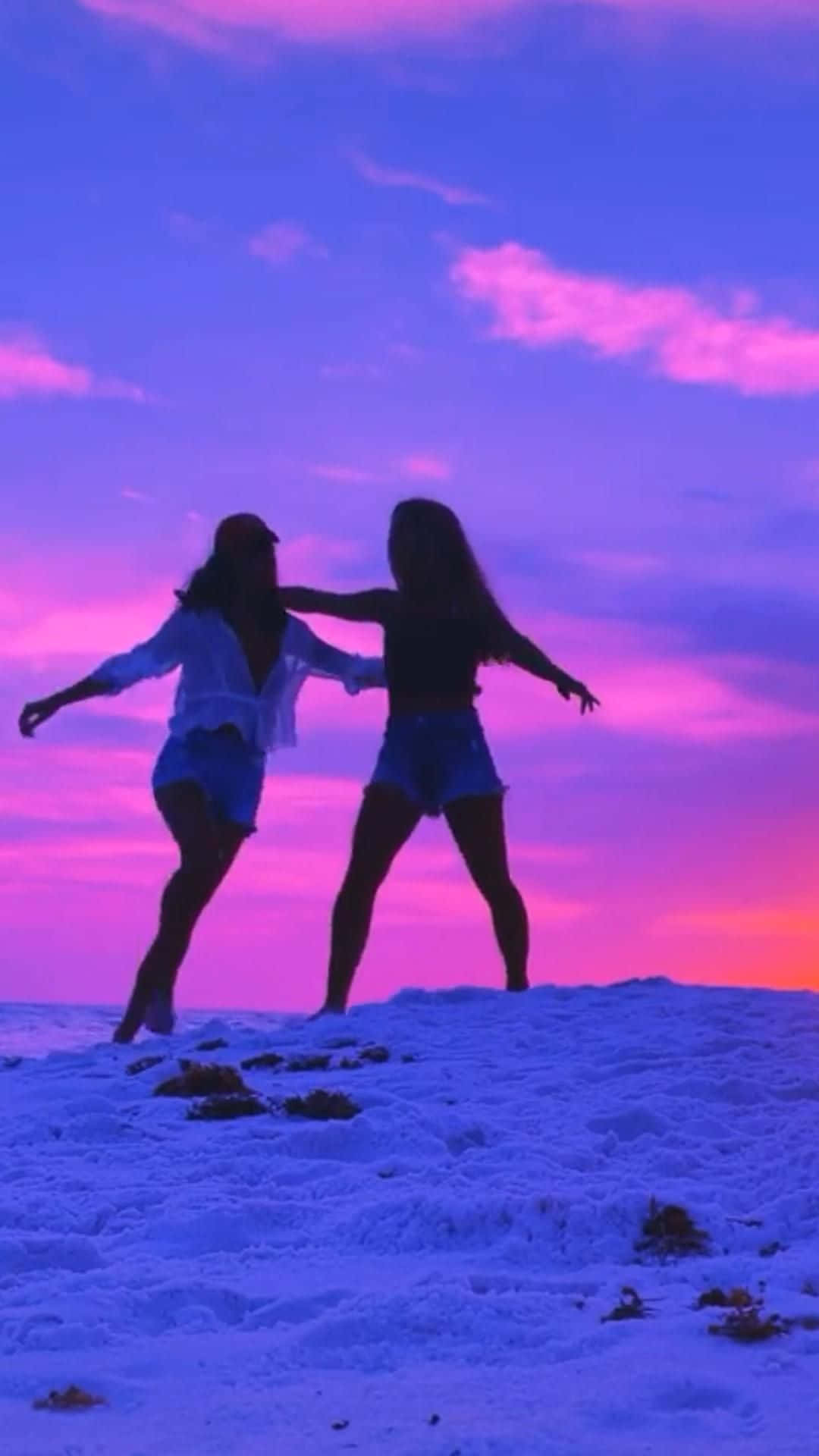 Best Friend Aesthetic 桌布 壁紙 — 兩個剪影女孩在雪山上，在充滿活力的紫色和粉紅色日落天空下快樂地跳舞。