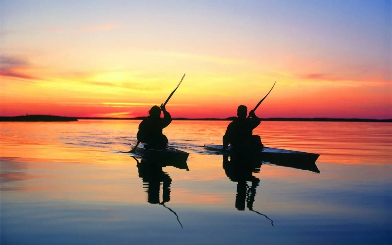 Rowing 桌布 壁紙 — 兩個剪影的皮划艇手划過玻璃般的湖面，熾熱的日落色彩完美地倒映在水面上。