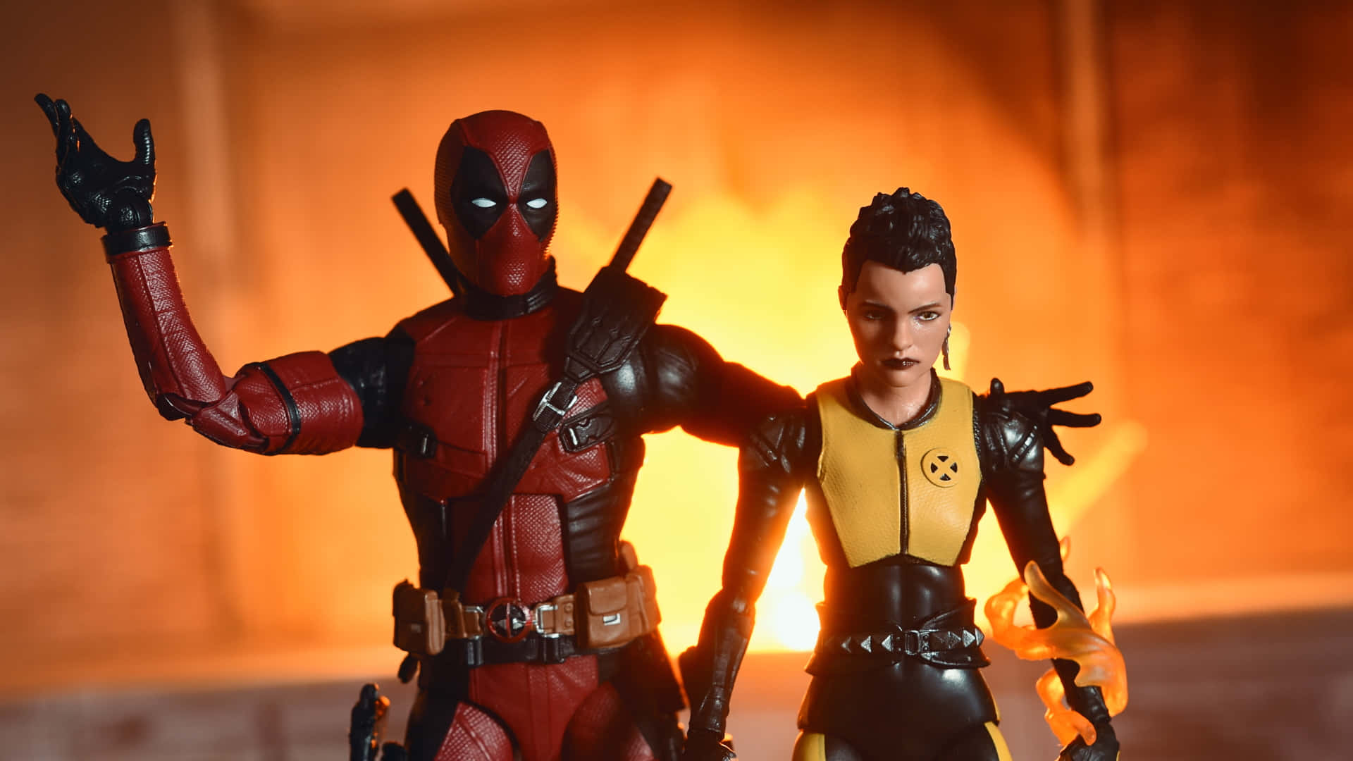 Deadpool And Negasonic Teenage Warhead 桌布 壁紙 — 兩個動作人偶死侍和多米諾站在火熱的橙色燈光中，帶有戲劇性的陰影和發光的眼睛。