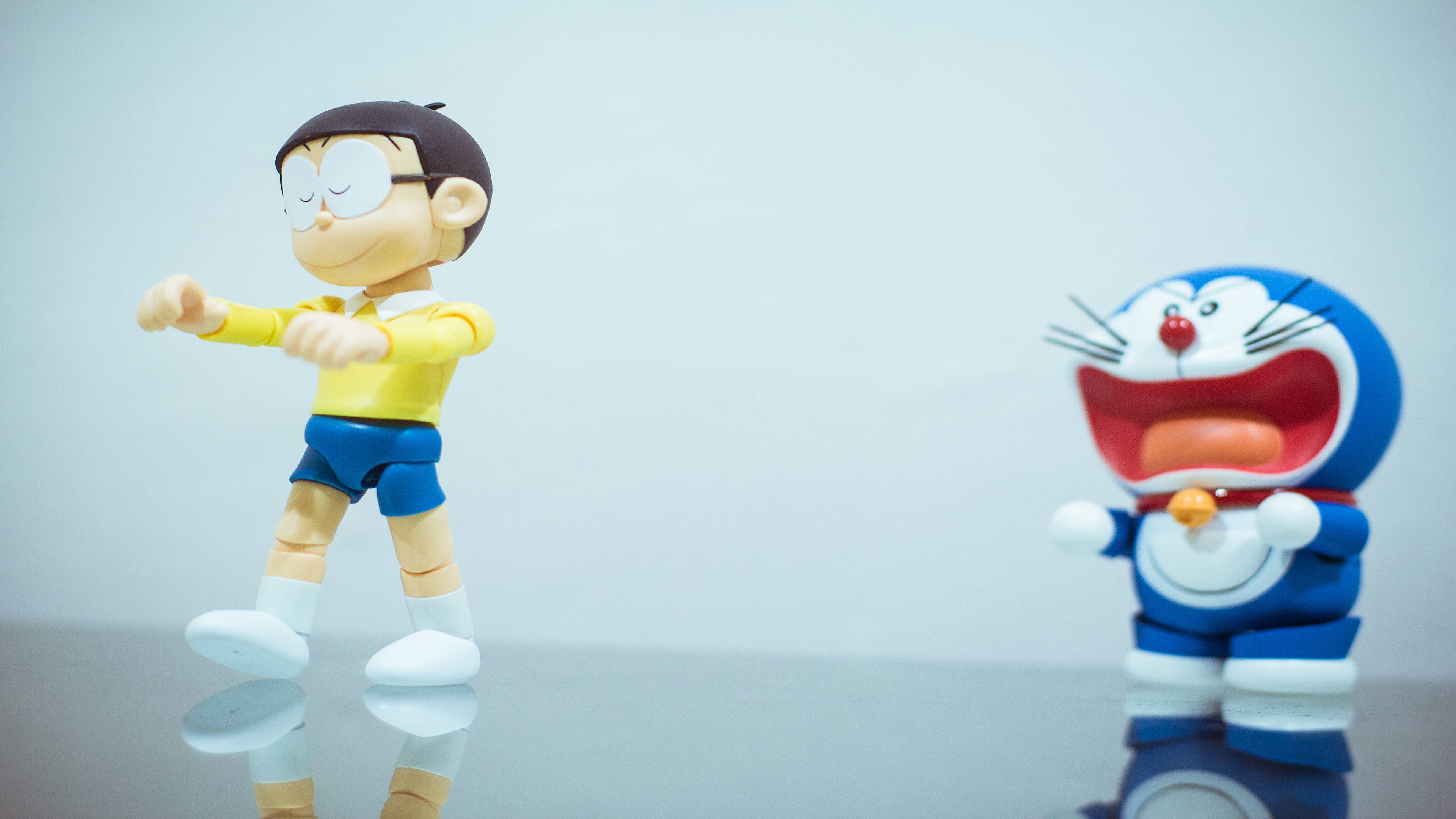 Doraemon 桌布 壁紙 — 兩個動漫公仔哆啦A夢和大雄在純色背景前的反光表面上擺姿勢。