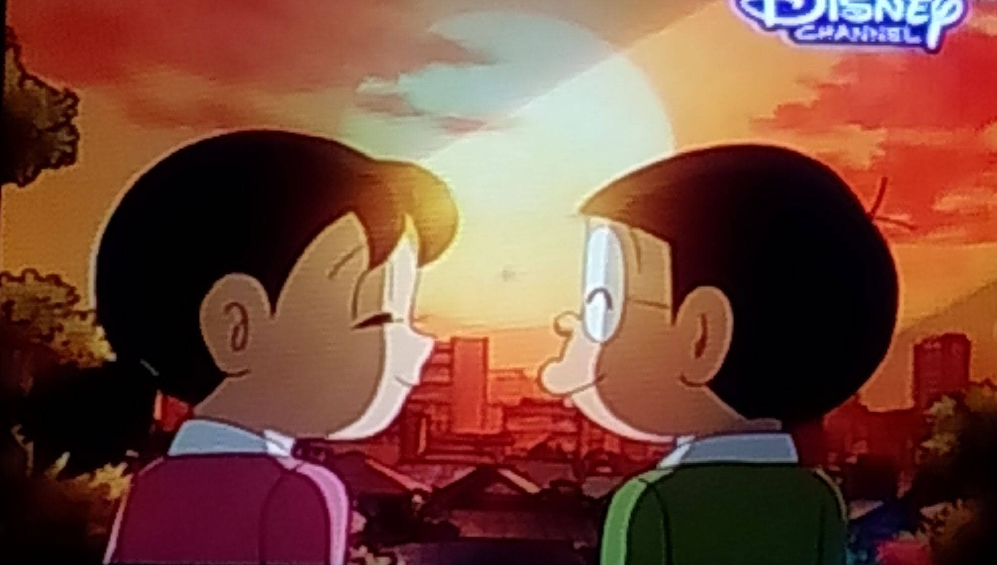 nobita 桌布 壁紙 — 兩個動漫男孩在溫暖的日落城市景觀中互相微笑，帶有Disney Channel標誌。