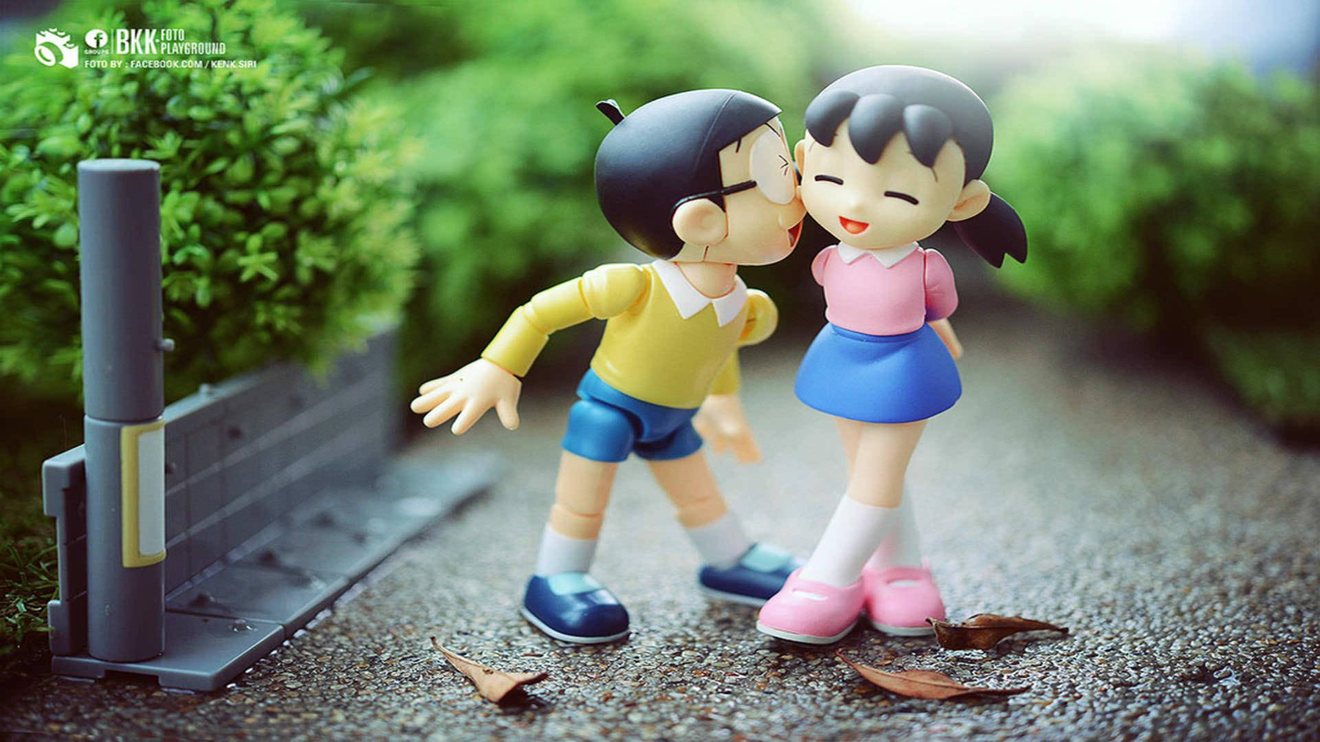Doraemon 桌布 壁紙 — 兩個動漫風格人偶在碎石小徑上甜蜜接吻，周圍綠意盎然。