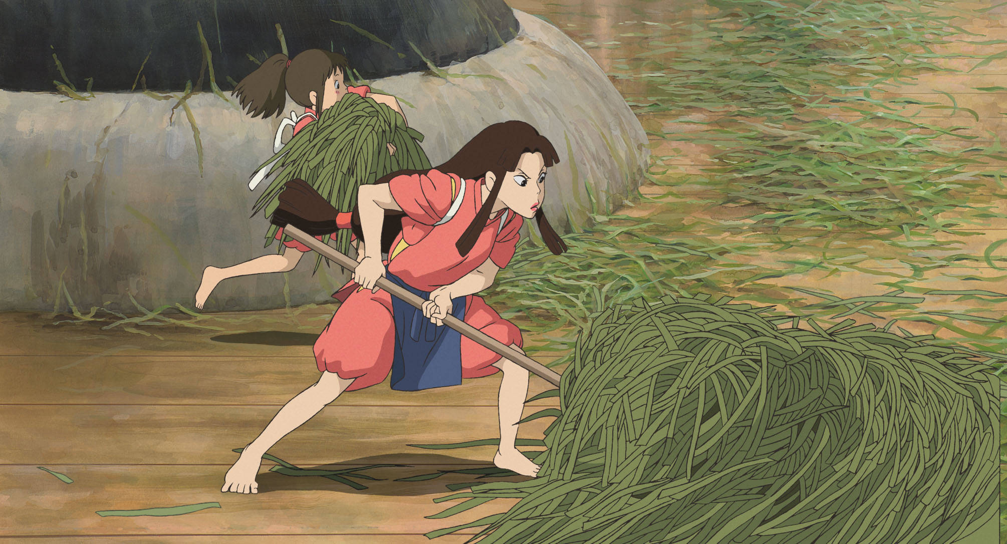 神隱少女 桌布 桌布 壁紙 — 兩個動畫女孩穿著紅色服裝，努力在石牆附近的木地板上推動一堆巨大的綠色蘆葦。