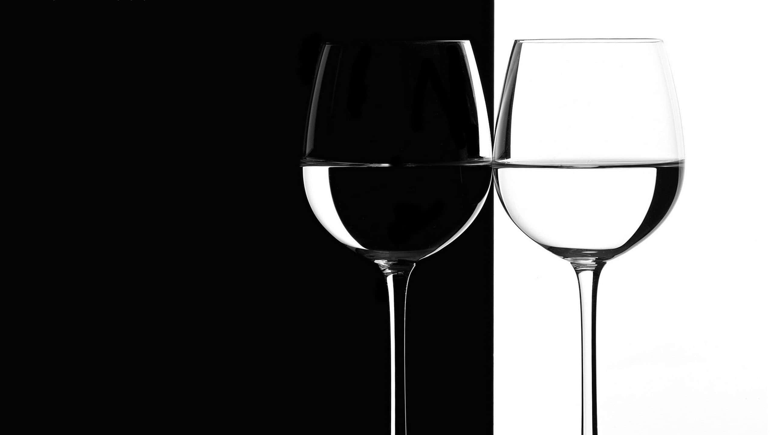 White Wine 桌布 壁紙 — 兩個半滿液體的酒杯立在黑白分明的背景前。