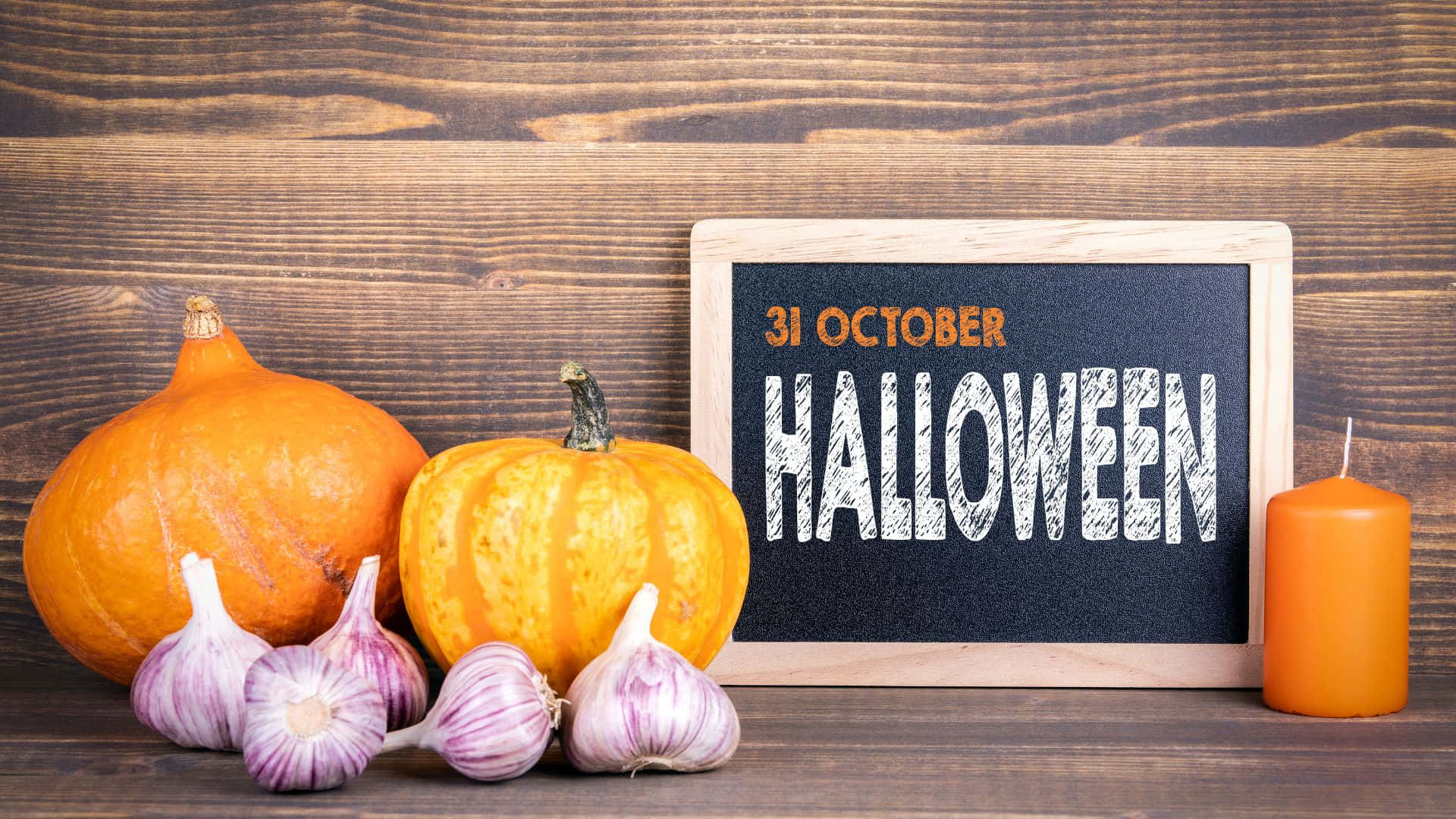 October 31st 桌布 壁紙 — 兩個南瓜和蒜瓣放在一塊寫著Halloween的黑板標誌旁，配上一支橙色蠟燭，置於鄉村風木頭上。