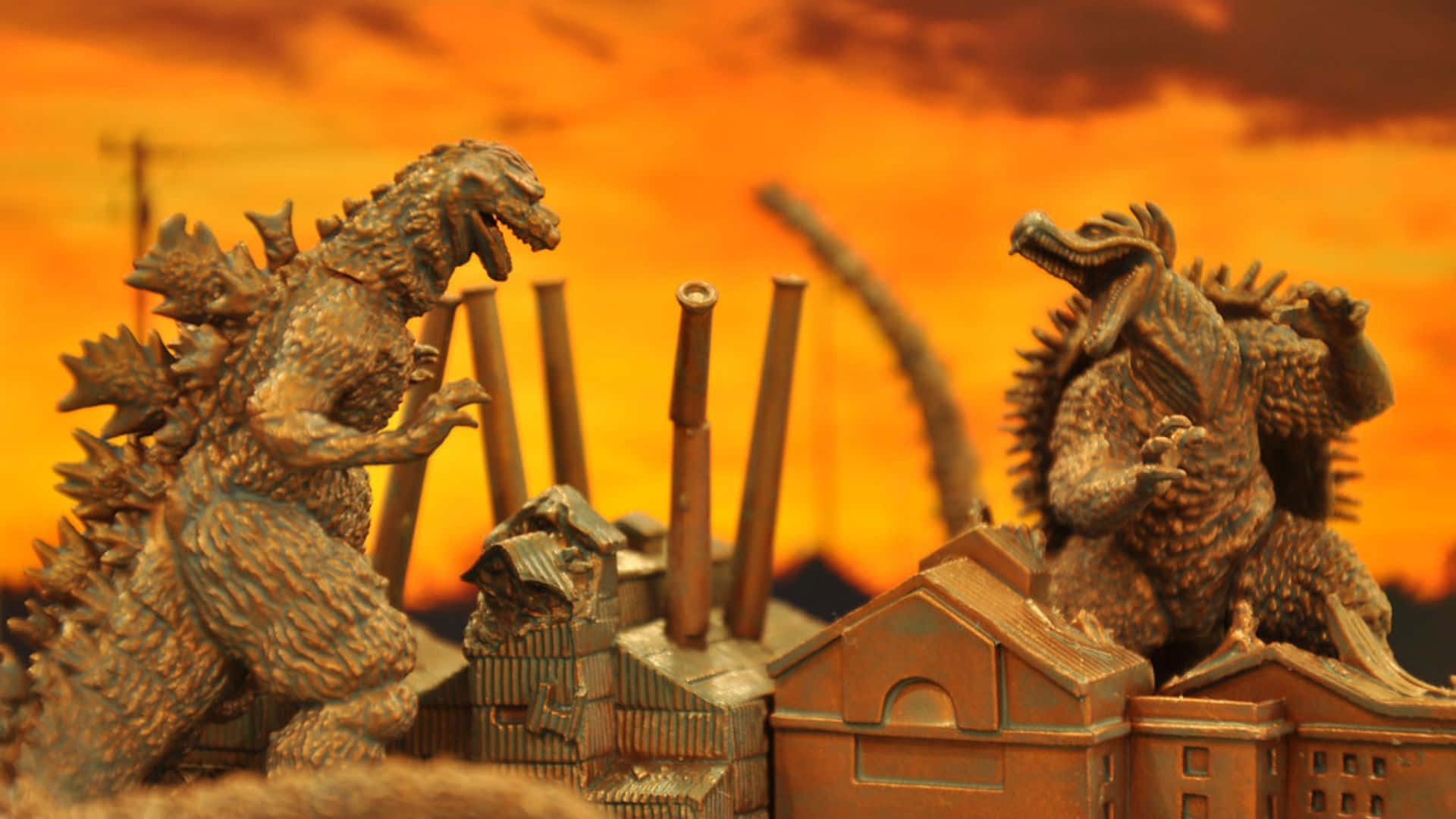 Godzilla Vs Anguirus 桌布 壁紙 — 兩個哥斯拉公仔在火熱的橙色日落天空下的微型建築物頂部碰撞。