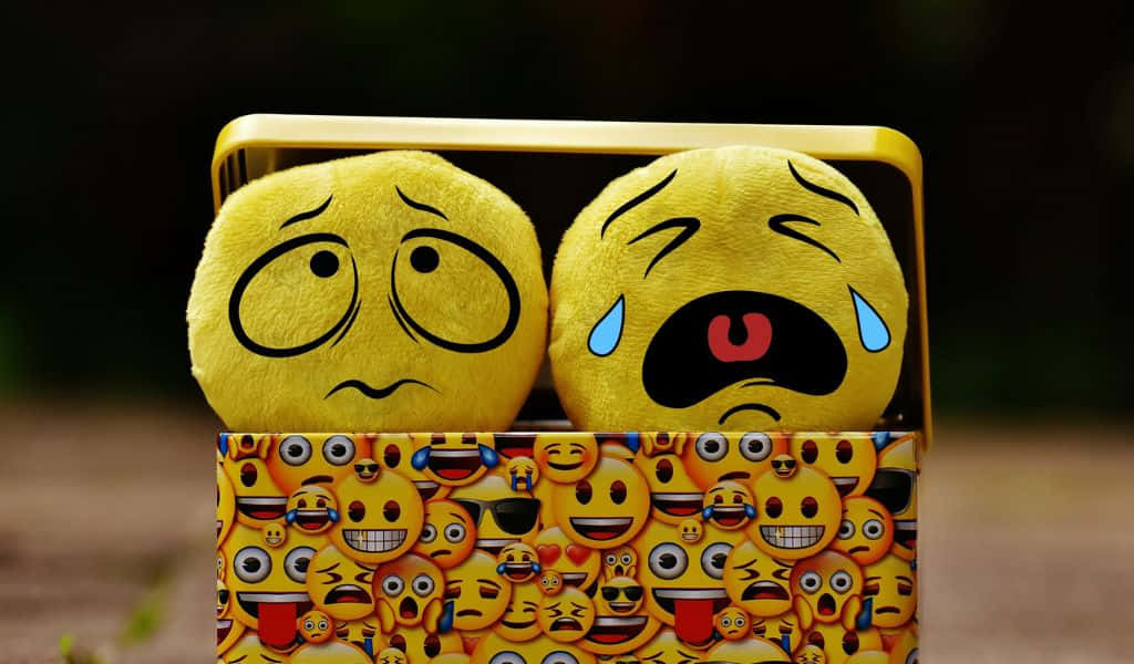 1024x600 桌布 壁紙 — 兩個哭泣的毛絨表情符號頭從一個裝滿色彩繽紛表情符號臉的罐頭中探出頭來。
