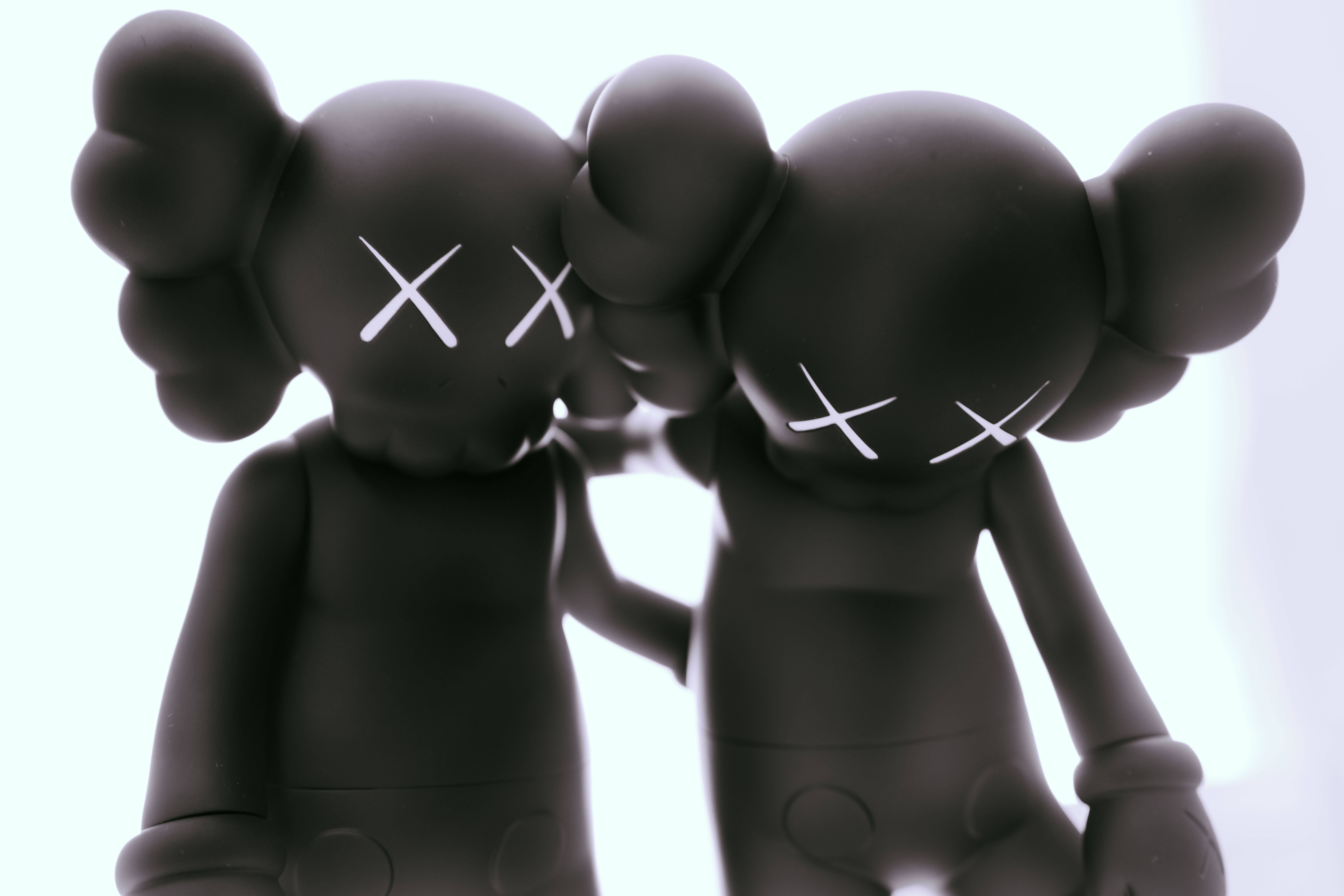 KAWS 桌布 壁紙 — 兩個啞光黑色KAWS人偶，帶有白色X眼睛，在明亮的白色背景上擁抱。
