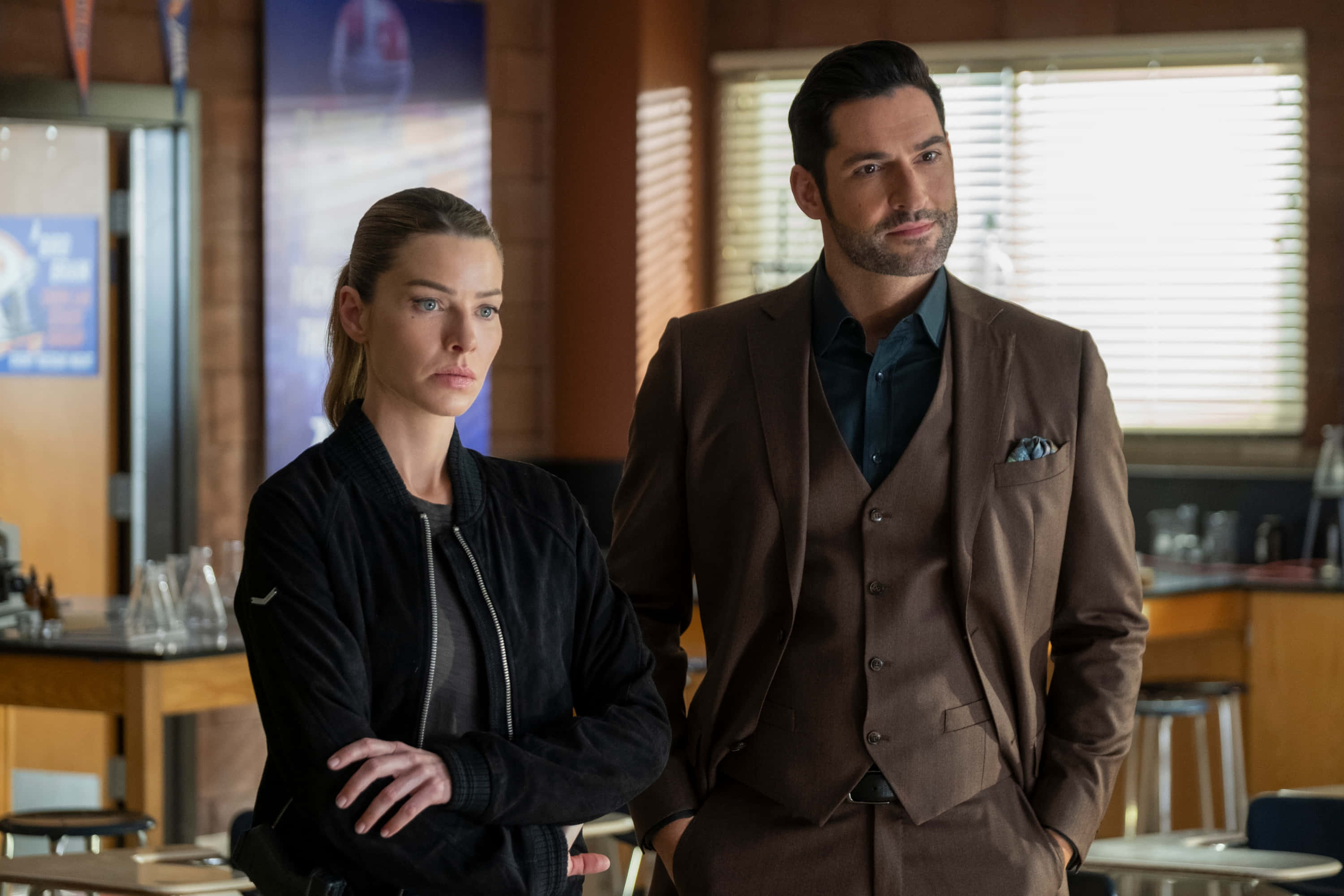 Lauren German 桌布 壁紙 — 兩個嚴肅的人站在一個燈光溫暖、有磚牆和木質卡座的餐廳裡。